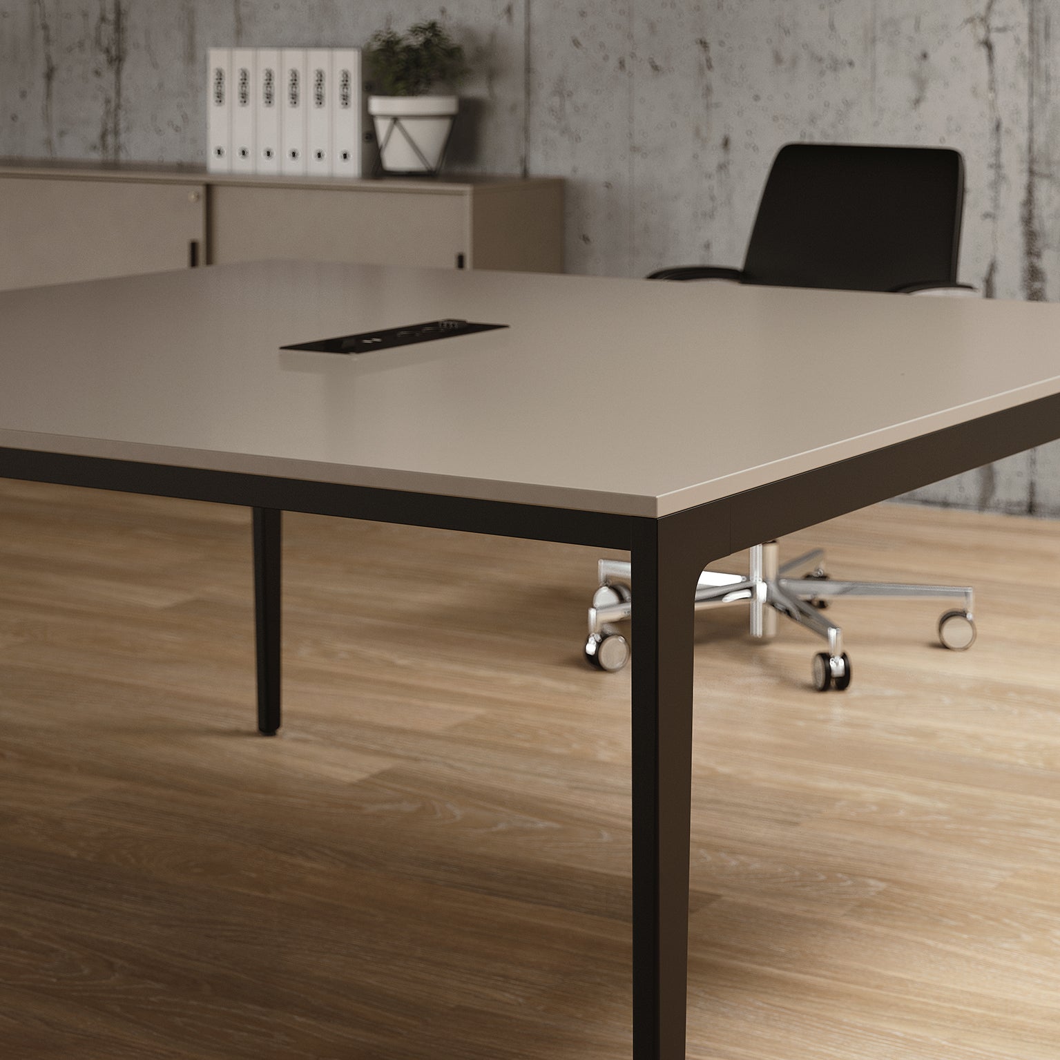 Un bureau moderne présente une grande Table de réunion modulables Alplus de Marco Zito, de couleur beige, avec gestion intégrée des câbles, une chaise à roulettes noire, des planchers en bois et un mur en béton. À l'arrière-plan se trouvent des armoires, une plante en pot et des classeurs blancs.