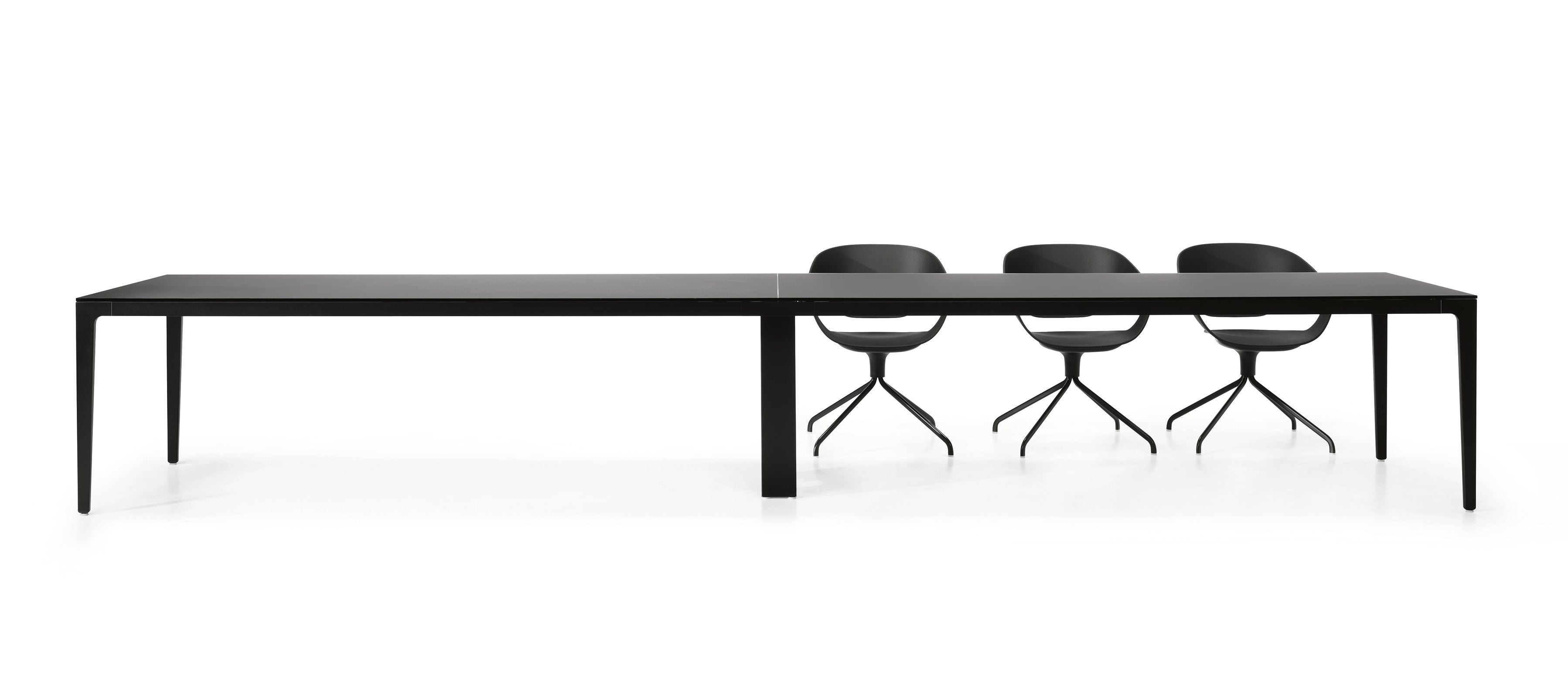 Les Tables de réunion modulables Alplus de Marco Zito- une table rectangulaire noire minimaliste avec gestion intégrée des câbles et pieds fins - sont associées à trois chaises noires modernes, placées sur un fond blanc uni.