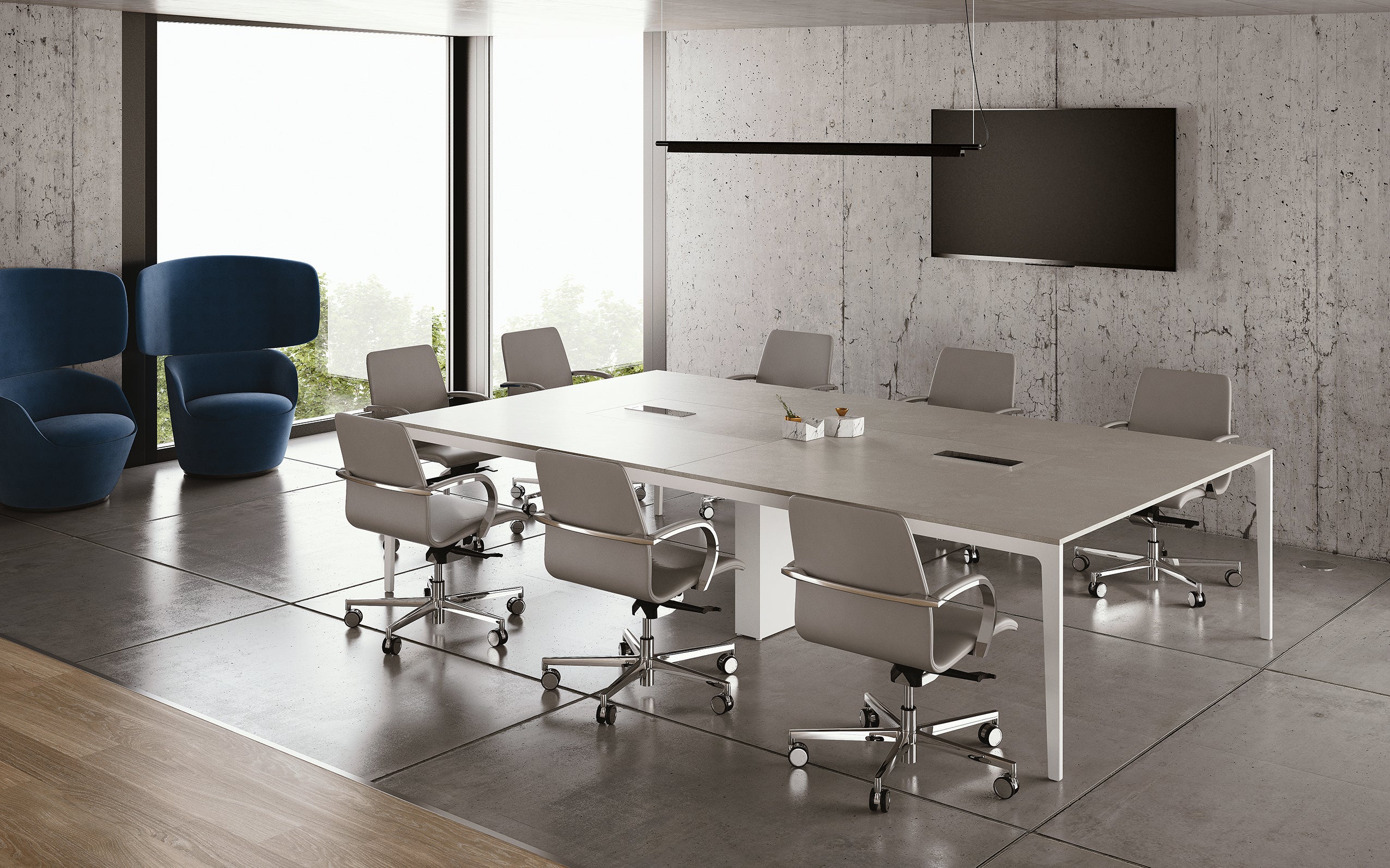 Une salle de conférence moderne avec les Tables de réunion modulables Alplus de Marco Zito, une grande table rectangulaire, huit chaises grises sur roulettes, une télévision murale, des murs en béton, de grandes fenêtres et deux chaises longues bleues dans le coin.