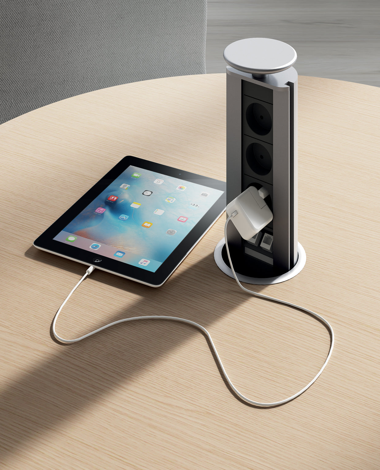 Une tablette se recharge sur un Attitudes Bureaux Tables de réunion Asset en bois clair, branché sur une prise électrique verticale modulable, partiellement surélevée, offrant des prises multiples et des configurations personnalisables.
