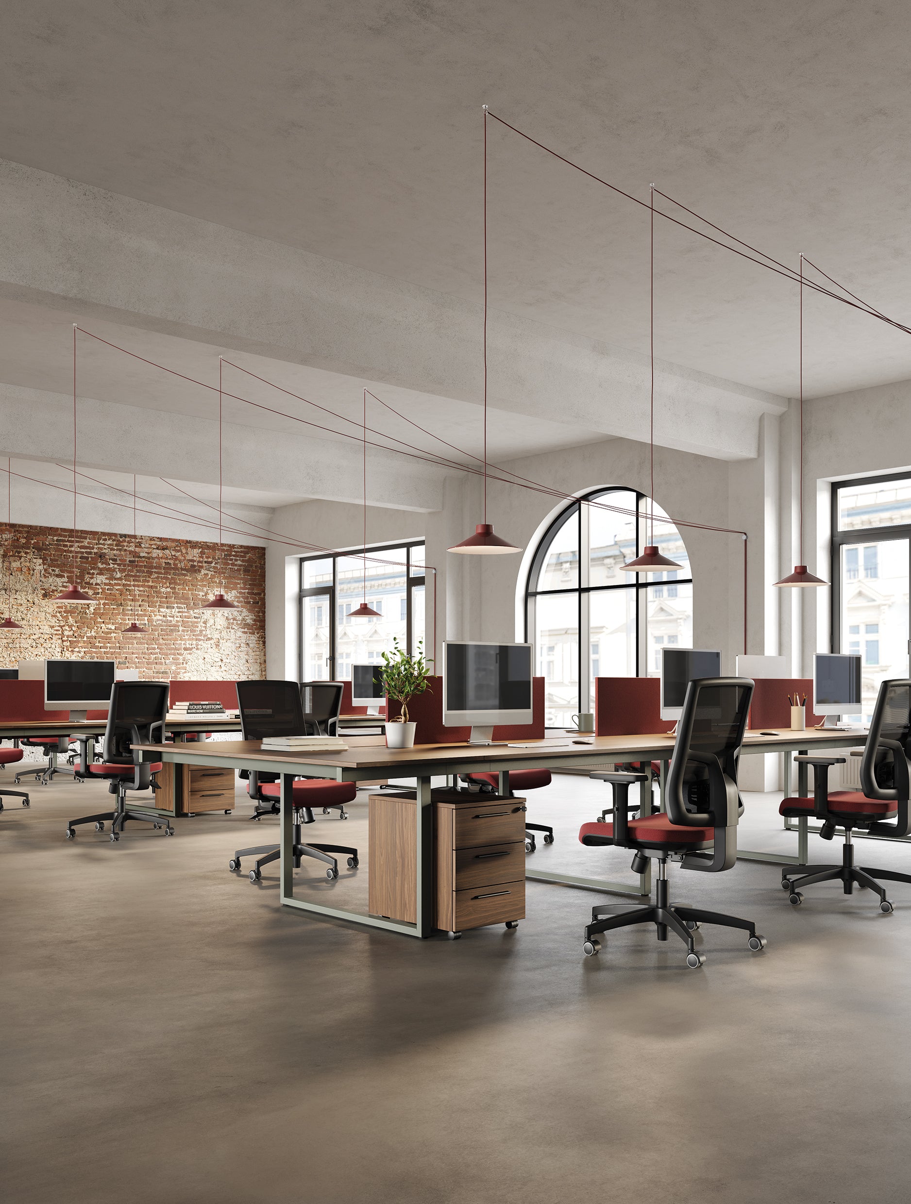 Le Bureau BE.1 de Progetto CMR est un espace ouvert avec des rangées de bureaux, des chaises rouges, des ordinateurs, des fenêtres cintrées pour la lumière naturelle, des murs en briques apparentes et des lampes suspendues rouges, alliant style industriel et solutions d'espaces de travail flexibles.