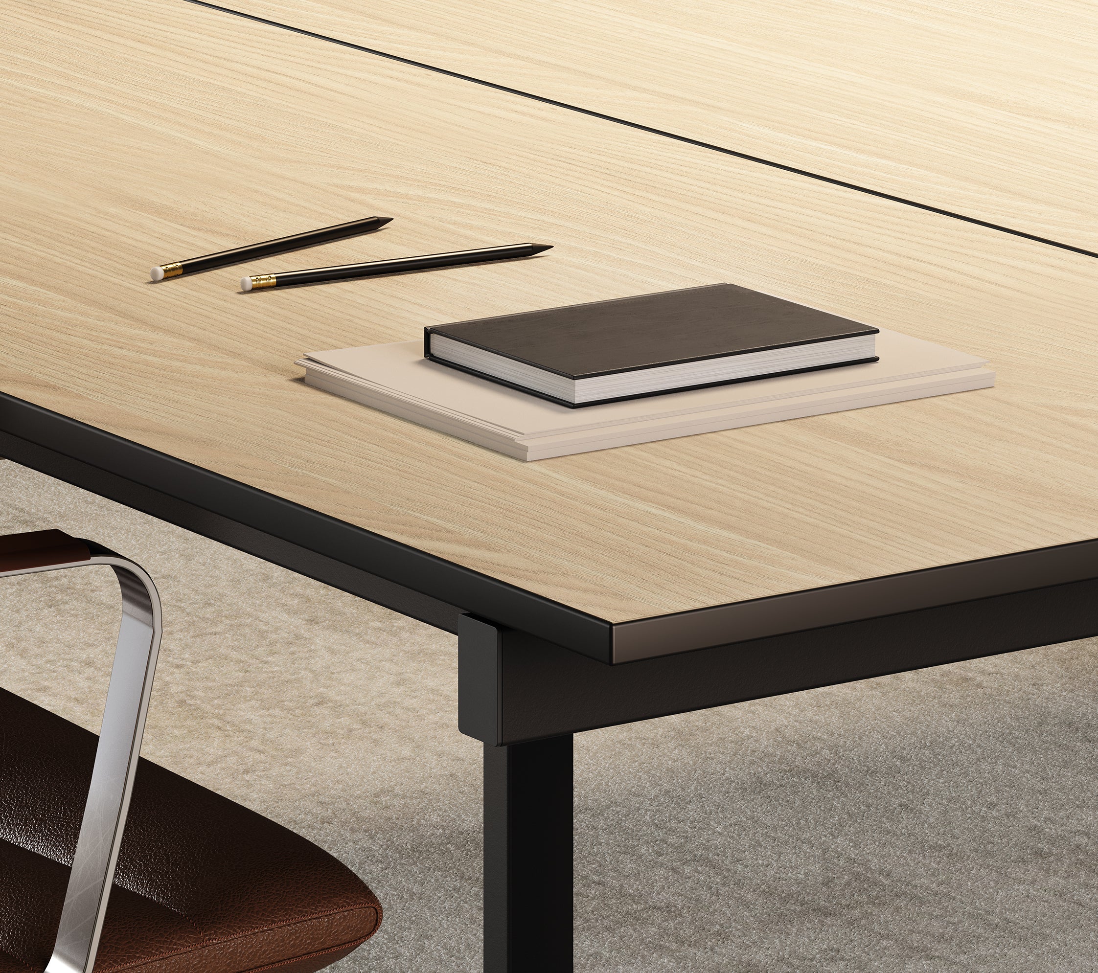 Un gros plan d'un bureau en bois présentant les Tables de réunion modulaires Be.1 de Progetto CMR met en évidence la modularité personnalisable, avec deux livres empilés, un cahier noir, des crayons et une partie d'une chaise en cuir marron visible sur le bord.