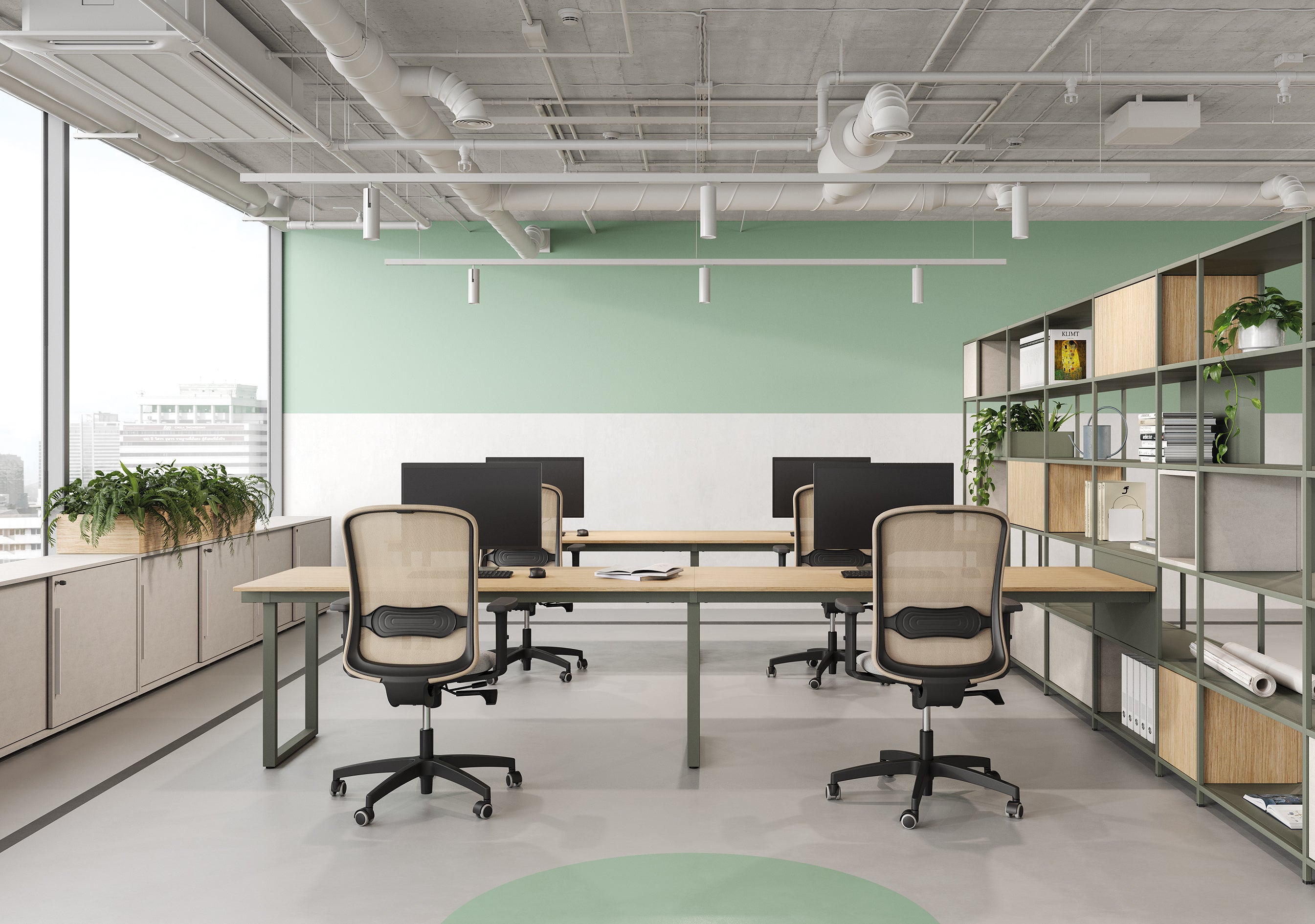 Le Bureau BE.1 de Progetto CMR comprend deux bureaux en bois avec des écrans d'ordinateur, quatre chaises ergonomiques, des murs verts, des plantes, de grandes fenêtres et des étagères ouvertes pour un espace de travail lumineux et flexible.