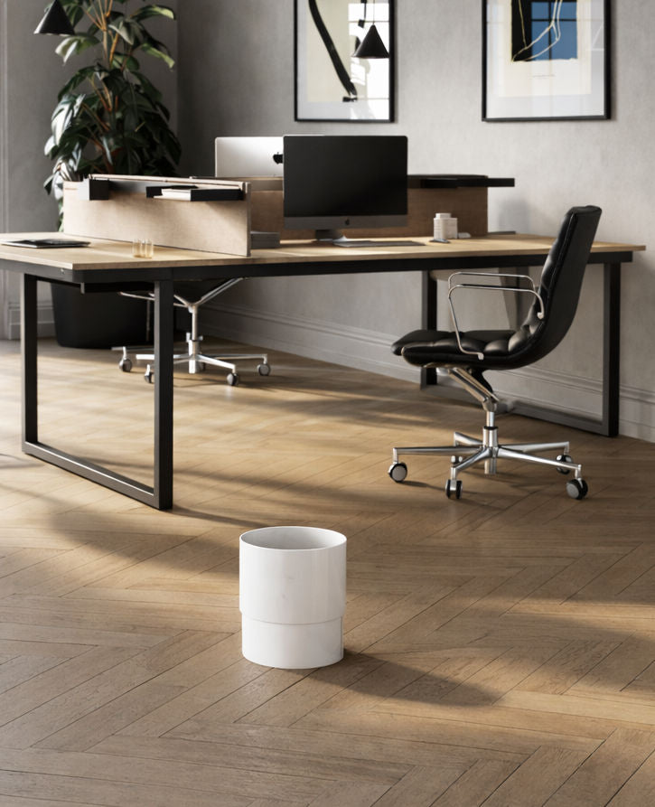 Bureau moderne avec sols en bois, deux bureaux avec ordinateurs et chaises, une grande plante dans le coin, un art mural abstrait et un Attitudes Bureaux Corbeille à papier au format 17L au premier plan.