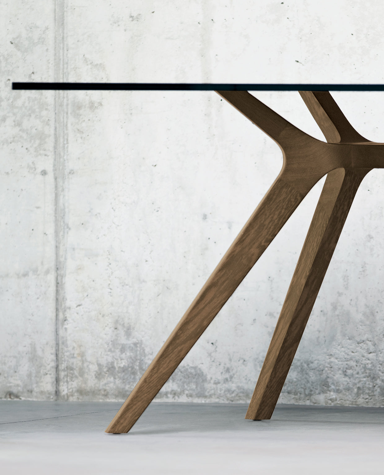 Gros plan sur les Tables de réunion Dr de Claudio Bellini, constituées de pieds angulaires en bois et d'un plateau en verre, sur fond de mur en béton.