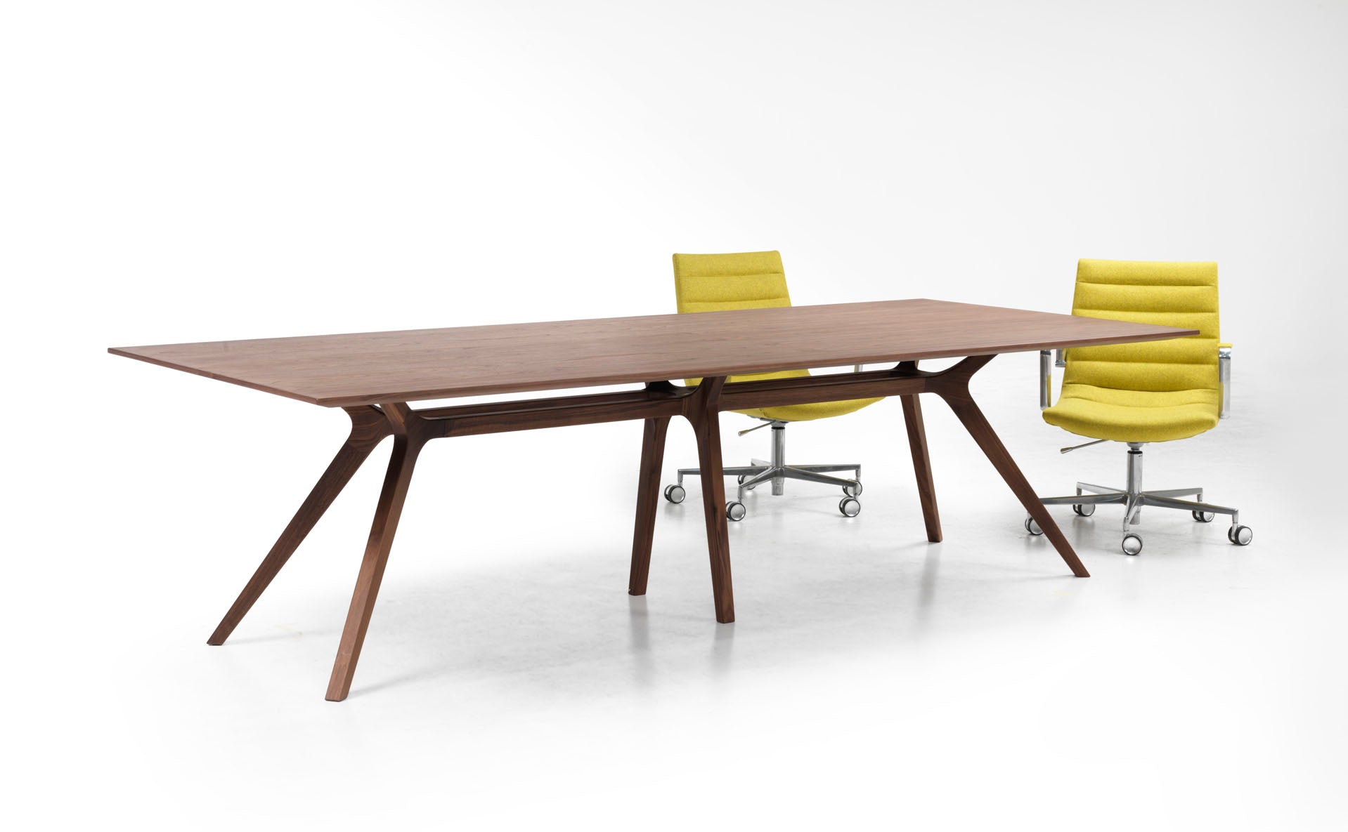 La table de réunion Dr de Claudio Bellini, au design moderne en bois rectangulaire et aux pieds angulaires, est associée à deux chaises de bureau jaunes pivotantes sur piétement métallique, sur un fond blanc uni.
