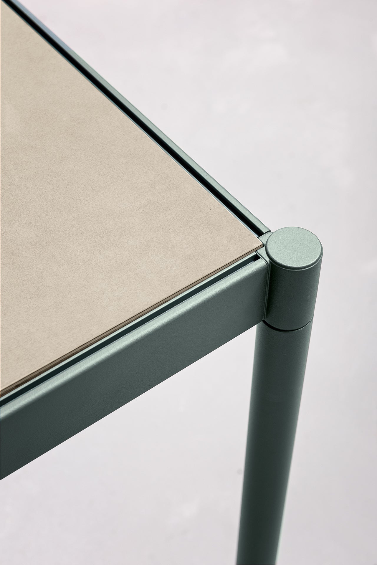 Gros plan sur une table Fluido d'Attitudes Bureaux, avec une structure en métal vert mat et un plateau beige clair. Ses lignes épurées et son design moderne mettent en valeur ce mobilier modulaire transformable sur un fond neutre.