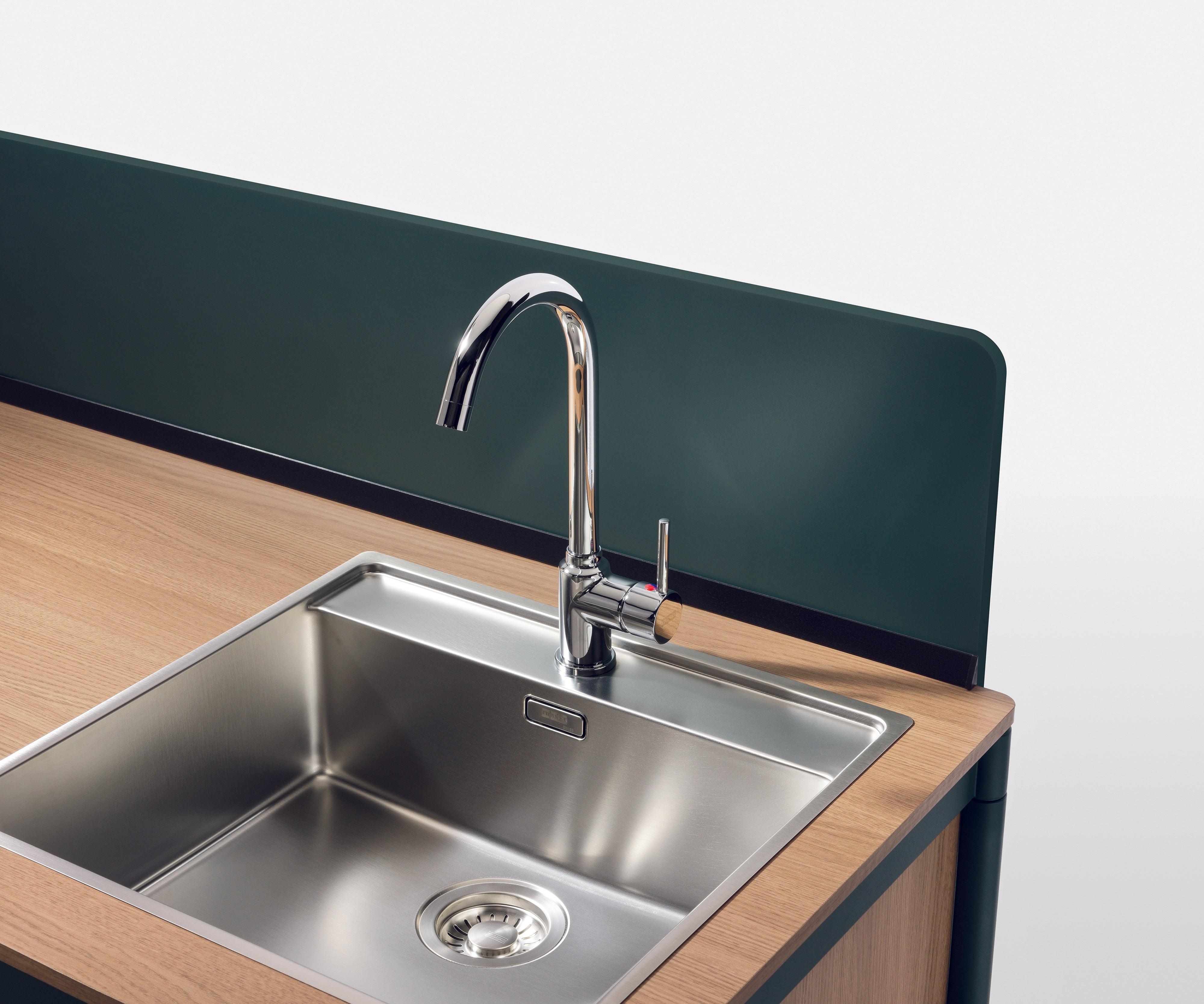 La kitchenette Fluido® d'Attitudes Bureaux présente un évier moderne avec un robinet chromé posé sur un plan de travail en bois clair, idéal pour un coin pause ou une kitchenette de bureau, et comprend un dosseret vert foncé. La poignée de l'évier propre est à droite.