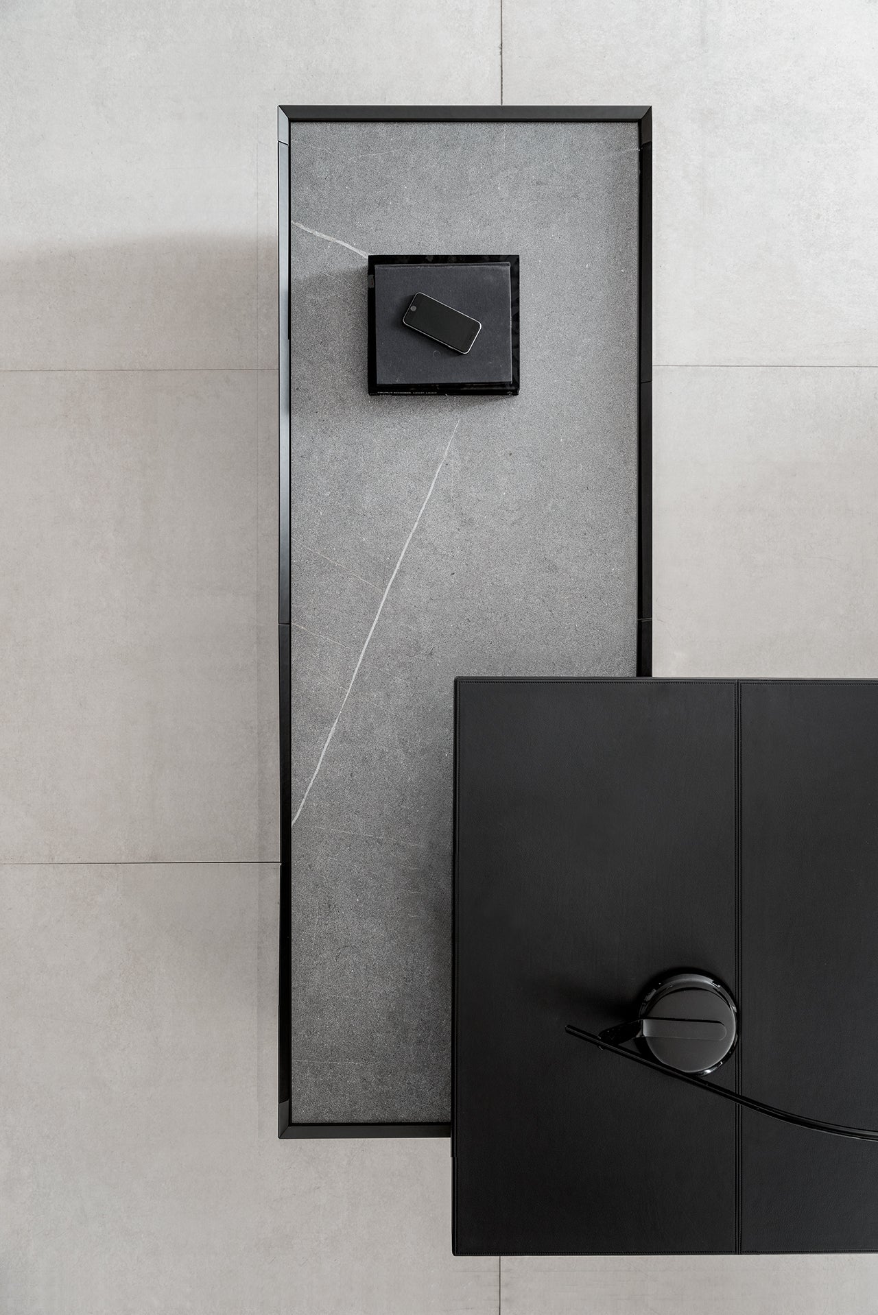 Un espace de travail minimaliste vu d'en haut présente Kyo by Attitudes Bureaux, une table rectangulaire en pierre grise avec des matériaux de première qualité, ainsi qu'un smartphone noir, un plateau et un bureau avec souris sur un sol carrelé gris clair.