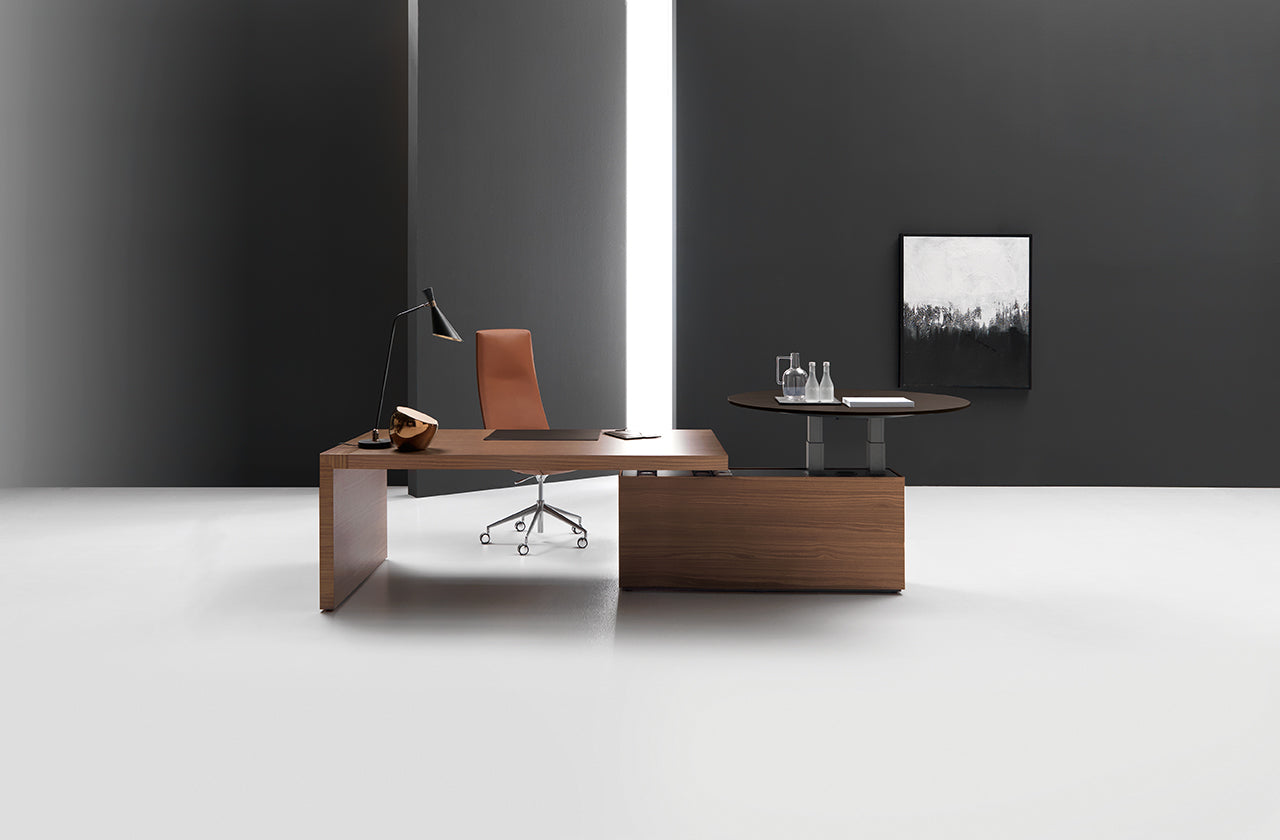 Ce bureau moderne et minimaliste met en valeur le bureau Kyo d'Attitudes Bureaux, associé à une chaise, une lampe, un téléphone et des objets en verre de couleur marron. Les murs sombres, une fenêtre étroite et un tableau abstrait mettent en valeur les matériaux haut de gamme de l'espace.