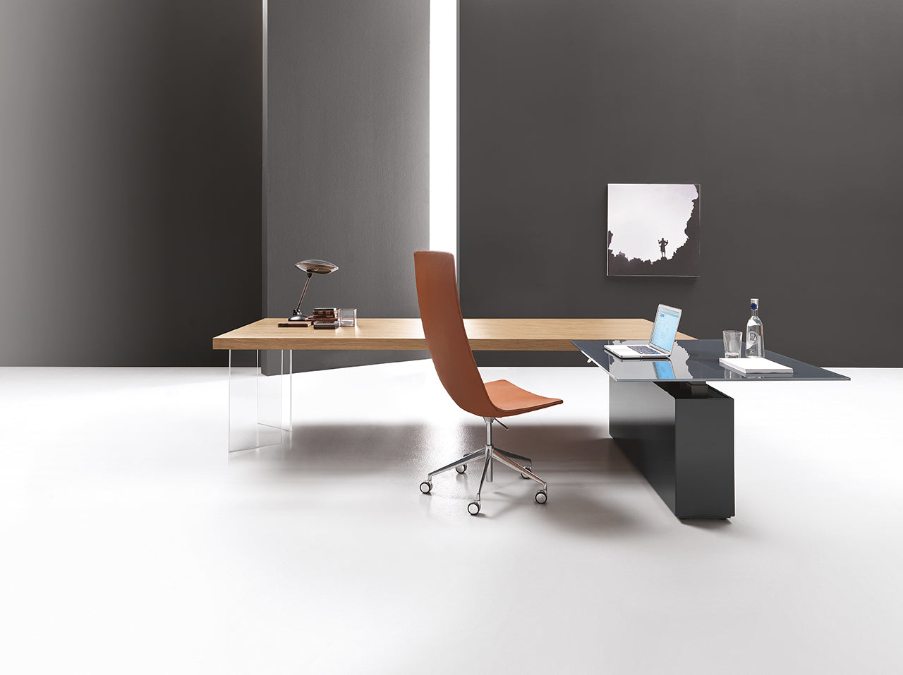 Bureau minimaliste avec le bureau Kyo d'Attitudes Bureaux, une chaise pivotante marron, un ordinateur portable, une lampe de bureau, une bouteille d'eau et une œuvre d'art sur un mur gris. Cette pièce lumineuse présente un décor contemporain épuré et des matériaux de première qualité.