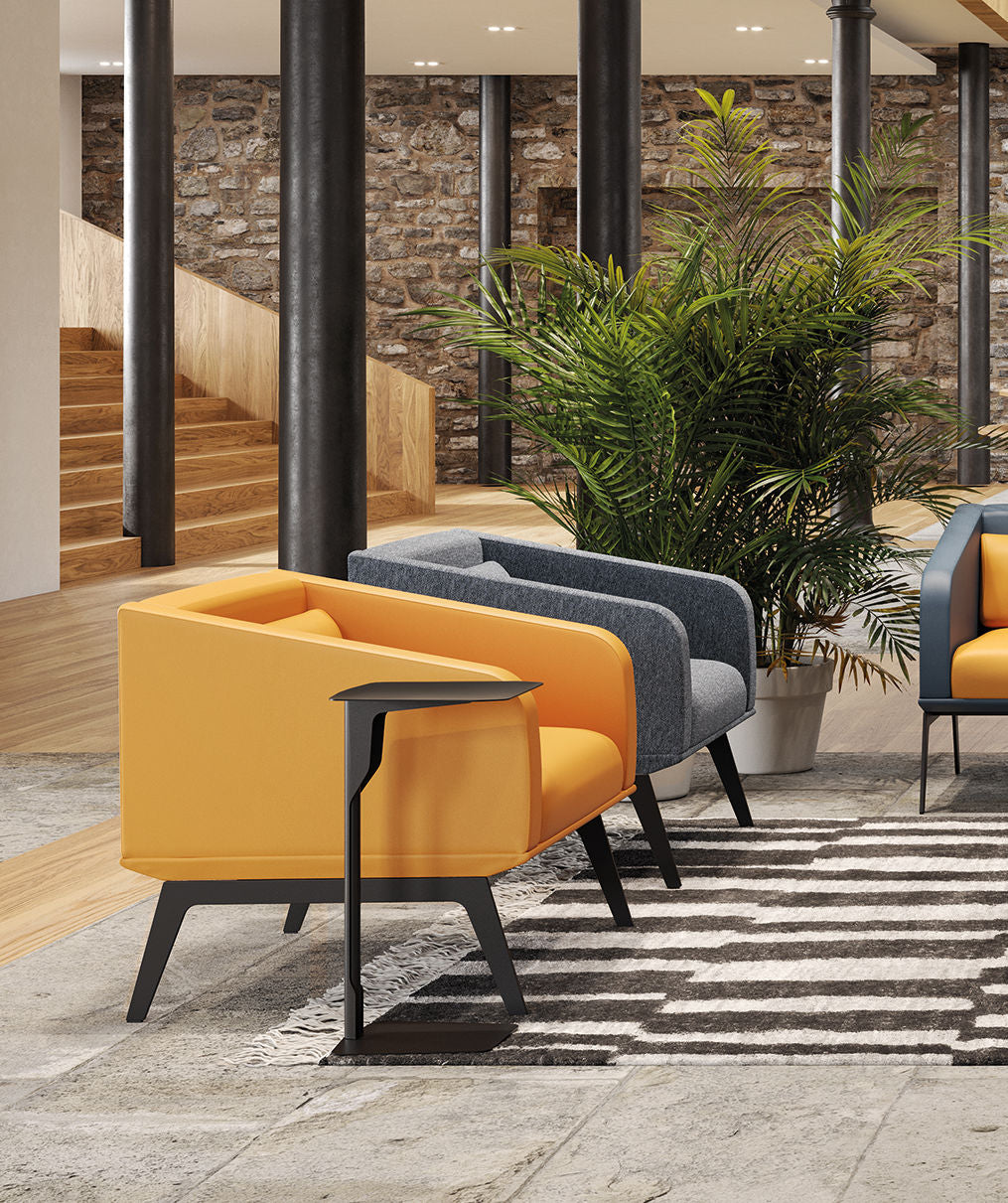 Salon moderne avec des fauteuils jaunes et gris, un tapis rayé, de la verdure en pot, des murs en pierres apparentes et la table en métal Luca Nichetto ; en arrière-plan, des escaliers en bois et des colonnes noires.