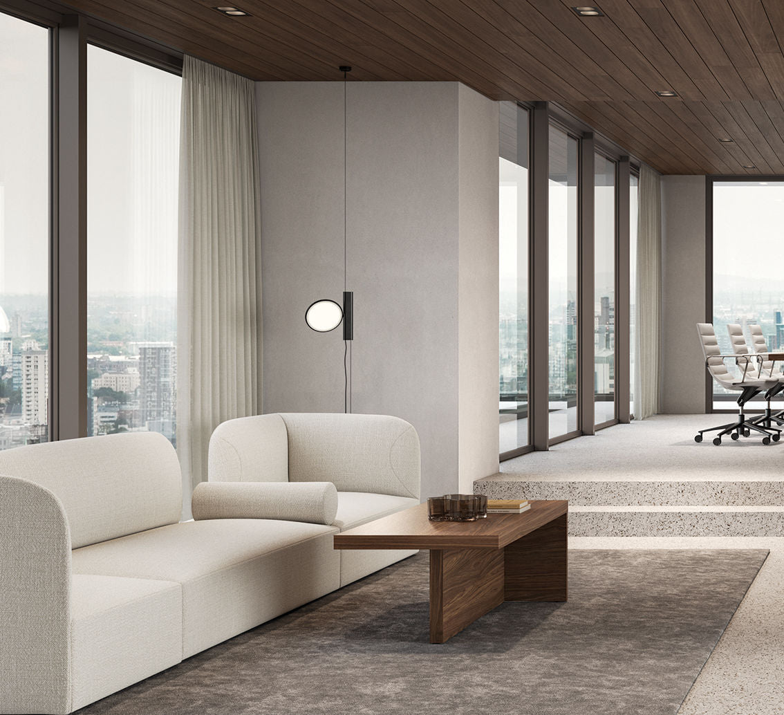 Un salon de bureau moderne avec un canapé crème, Table basse design Mux70 de Stefano Boeri Interiors, et de grandes fenêtres avec vue sur la ville. À l'arrière-plan, une salle de conférence est équipée de chaises et d'une longue table de la marque, derrière des murs en verre.