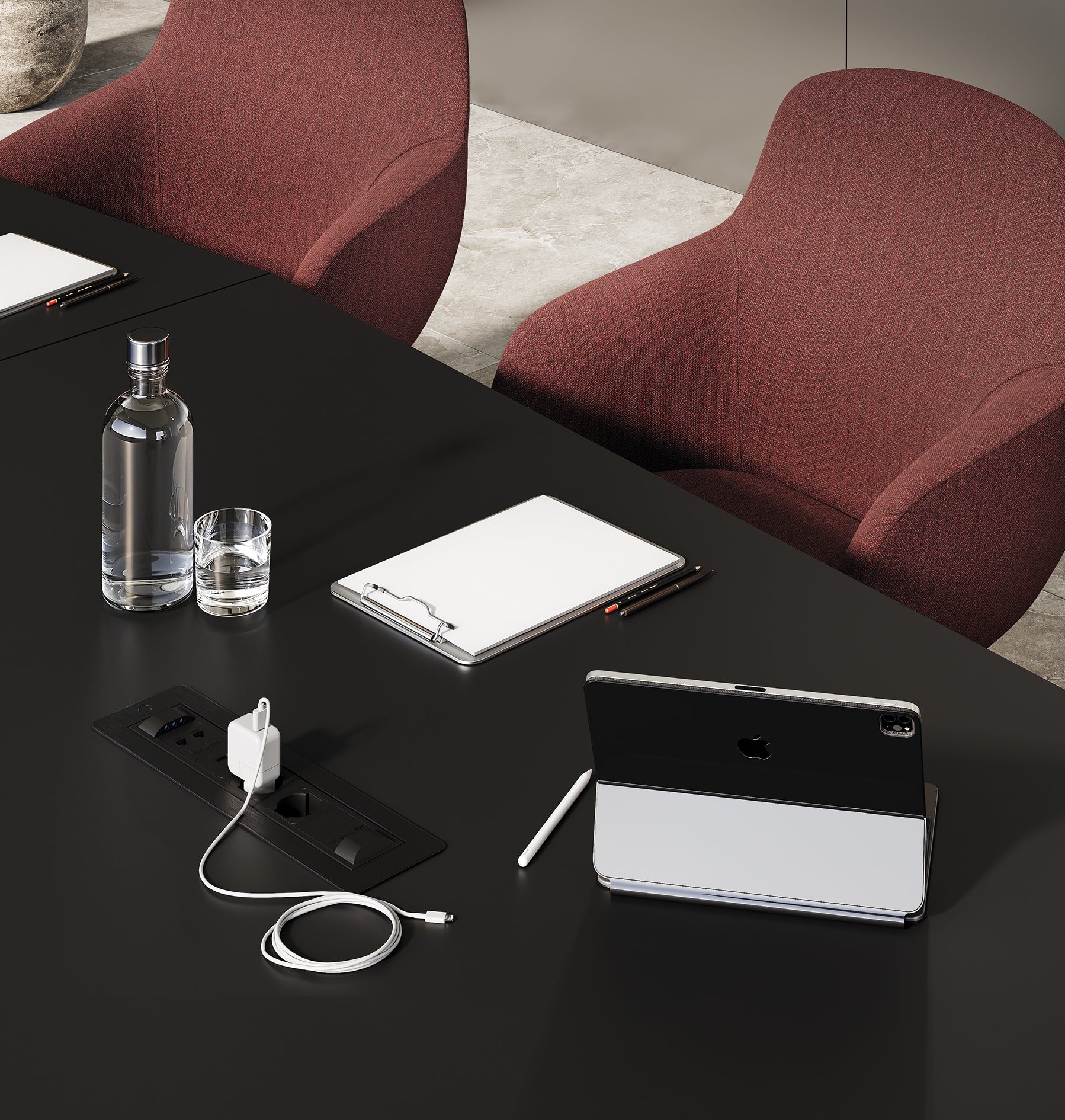 Une table de réunion Mux70 de Stefano Boeri Interiors présente une bouteille d'eau, un verre, un presse-papiers et une tablette avec stylet. Deux chaises bordeaux sont assises à côté, et un câble de recharge est connecté à la prise électrique intégrée.