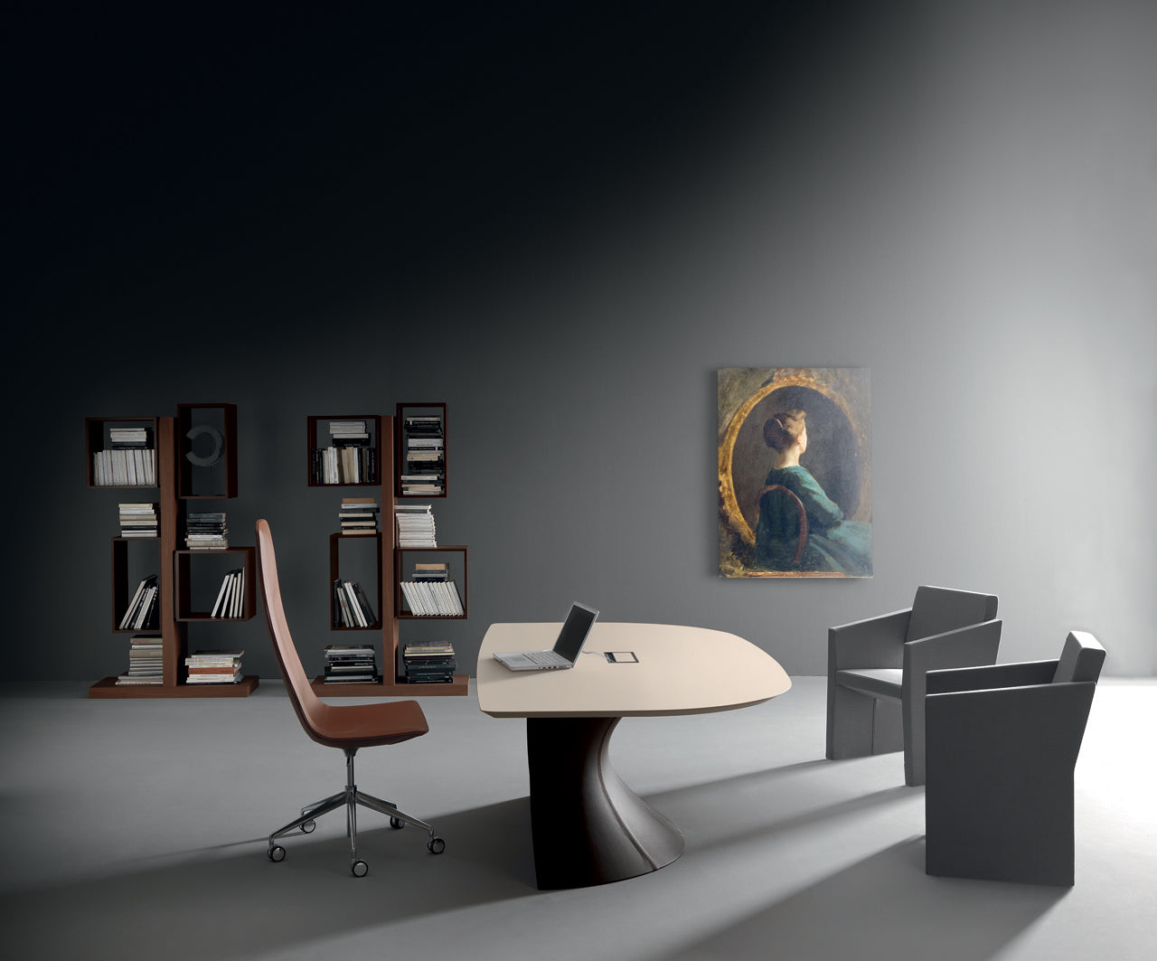 Un bureau moderne avec le bureau Ola d'Attitudes Bureaux composé d'un piétement en ellipse, d'une chaise pivotante marron, de deux fauteuils gris, d'étagères remplies de livres, d'un ordinateur portable posé sur le bureau et d'un portrait de femme à la lumière tamisée.