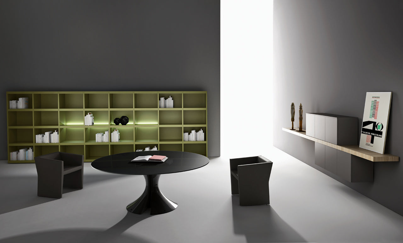 Bureau minimaliste présentant Ola d'Attitudes Bureaux : murs gris, table ronde noire à base elliptique, trois chaises modernes, grande étagère verte avec des livres, des armoires murales et de la décoration sur une étagère flottante près d'une fenêtre verticale lumineuse.