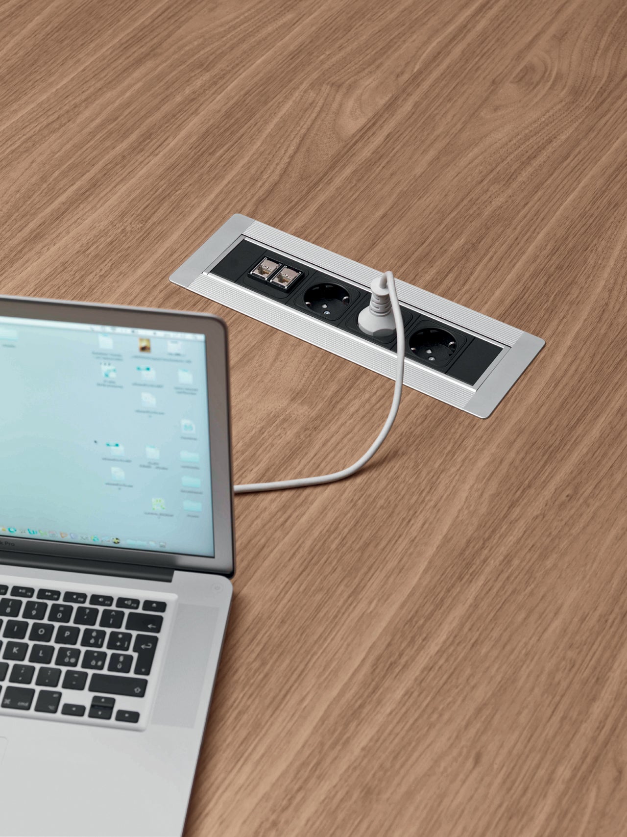 Un panneau de prises Attitudes Bureaux Ola est installé dans un bureau en bois avec une base en forme d'ellipse, comportant des prises de courant et des ports réseau. Un ordinateur portable est connecté, son écran est partiellement visible avec des dossiers et des icônes affichés.