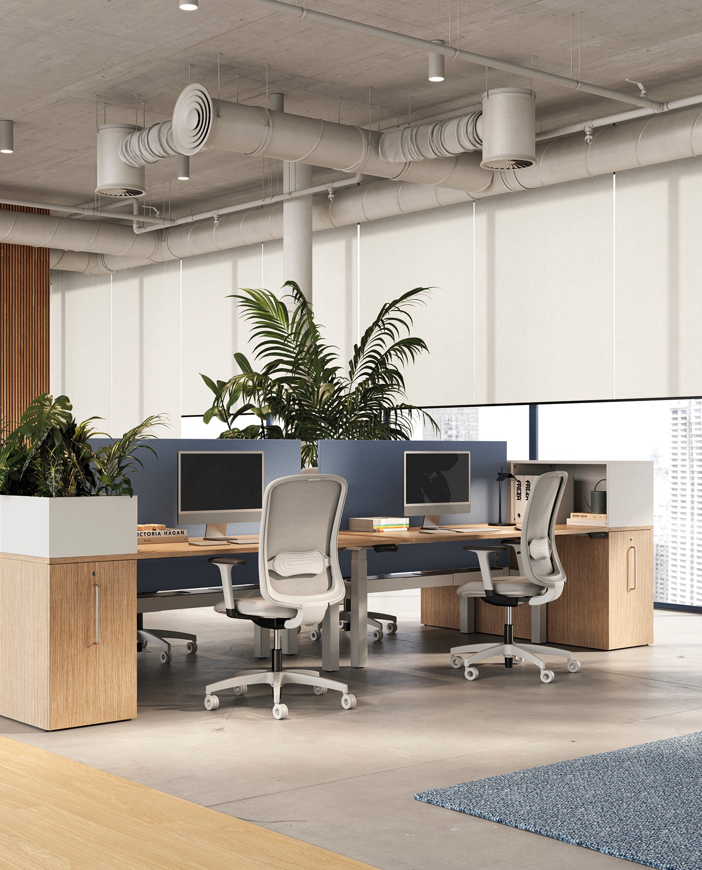 Un bureau moderne à aire ouverte comprend quatre chaises ergonomiques, des bureaux d'ordinateur, des Attitudes Bureaux Orgatower rangement compact et intelligent, de grandes plantes en pot, des meubles en bois clair et des fenêtres allant du sol au plafond avec des stores à enroulement pour une ambiance ouverture frontale.
