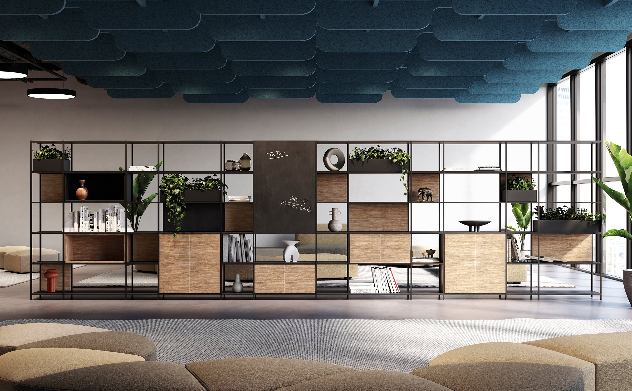 Un espace de bureau moderne dans lequel Attitudes Bureaux Bibliothèque de bureau modulaire Phylo présente des livres et des objets de décoration. Des panneaux acoustiques bleus sont suspendus au-dessus de la tête, de grandes fenêtres inondent la pièce de lumière et des sièges neutres ajoutent une touche de design haut de gamme.