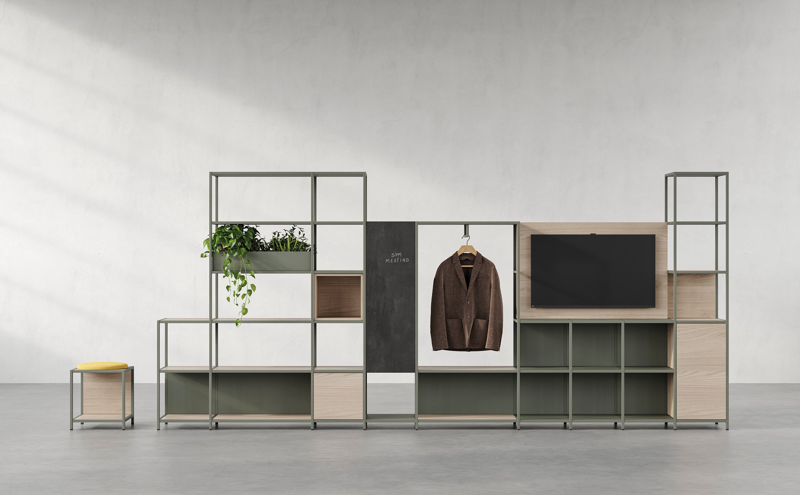 La Bibliothèque de bureau modulaire Phylo d'Attitudes Bureaux présente des cadres métalliques, des panneaux de bois clair, un téléviseur monté, une plante en pot, une veste marron suspendue et un tabouret à coussin jaune contre un mur gris uni dans un espace moderne.