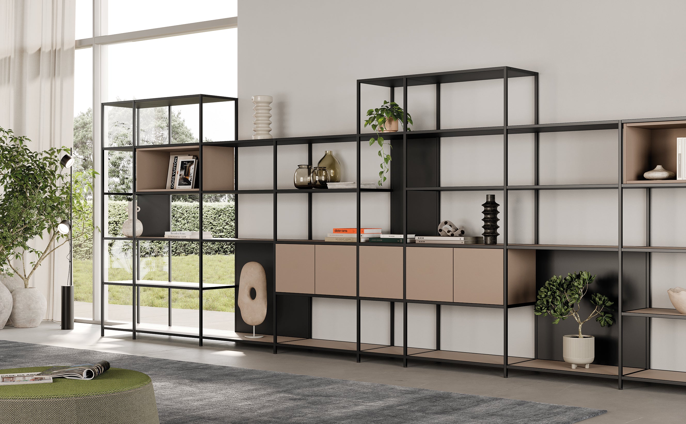 Dans un salon moderne, de grandes bibliothèques modulaires Phylo d'Attitudes Bureaux accueillent livres, plantes et objets de décoration. La lumière du soleil pénètre par de hautes fenêtres dans cet espace minimal et élégant, avec une touche haut de gamme ; la verdure est visible à l'extérieur.