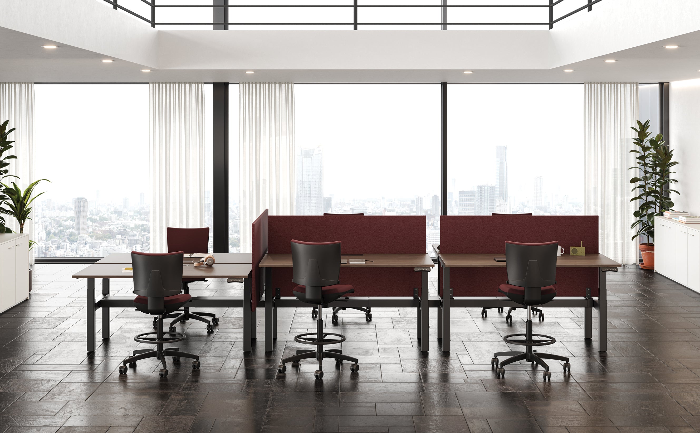 Bureau ouvert moderne avec quatre Attitudes Bureaux Pop AD bureaux réglables en hauteur et des chaises par paires, divisés par des panneaux rouges. De grandes fenêtres, des rideaux blancs, des plantes en pot et un carrelage noir épuré renforcent l'aspect lumineux et minimaliste de l'ensemble.