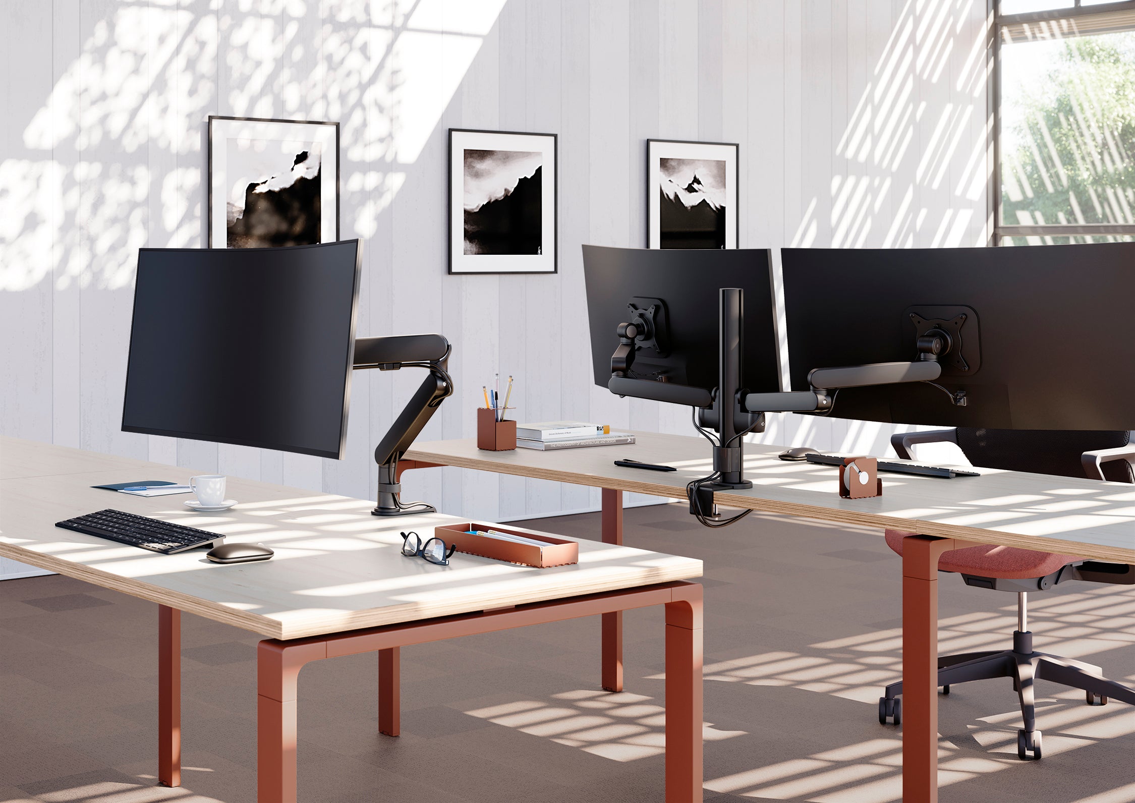 Dans un bureau moderne, deux bureaux sont équipés d'écrans Plug et Play Duo d'Attitudes Bureaux Supports pour des espaces de travail ergonomiques. La lumière du soleil projette des ombres sur un mur blanc décoré de trois photos encadrées en noir et blanc.