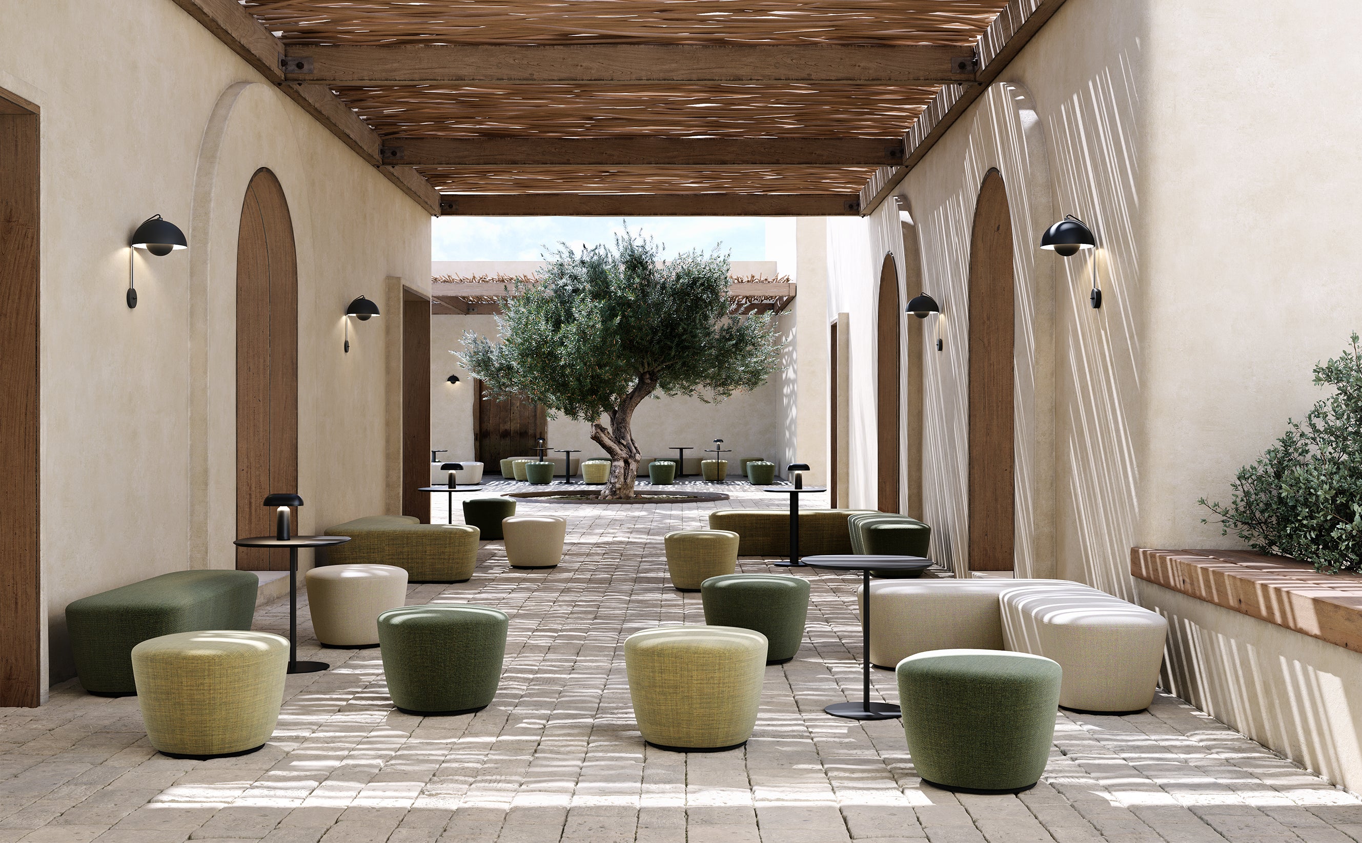 Un patio moderne avec des murs en pierre claire, une pergola en bois, des poufs RADAR de Claesson Koivisto Rune CKR en vert et beige, de petites tables noires et un olivier. La lumière douce du soleil projette des ombres sur le sol pavé.