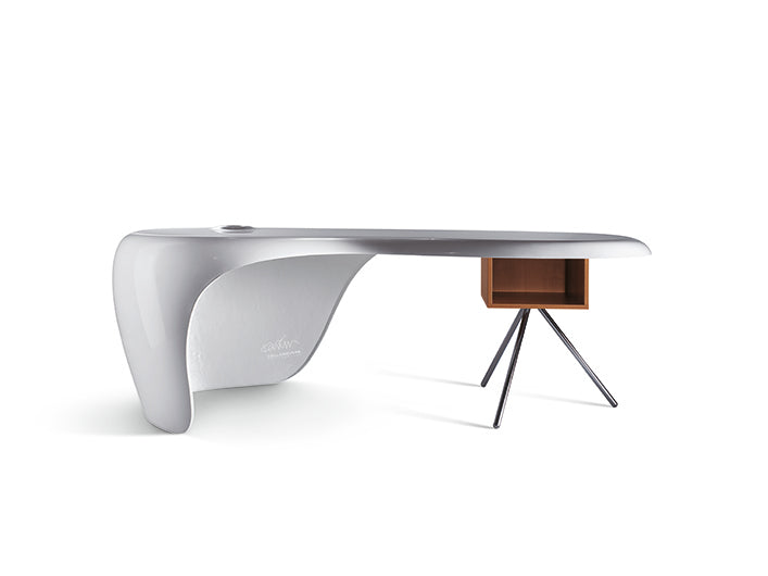 Le bureau UNO de Karim Rashid présente un design asymétrique moderne avec une base blanche lisse et incurvée à gauche et un coffre de rangement en bois avec trois pieds en métal à droite, parfait pour une décoration de bureau élégante sur un fond blanc uni.