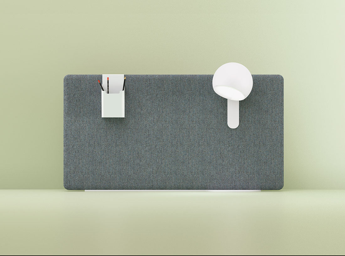 Espace de travail minimaliste avec Cloisons et écrans acoustiques MADISON gris d'Attitudes Bureaux. Une lampe blanche est fixée à droite, et un support blanc contenant des stylos noirs et rouges se trouve à gauche. L'arrière-plan est un mur vert pâle.