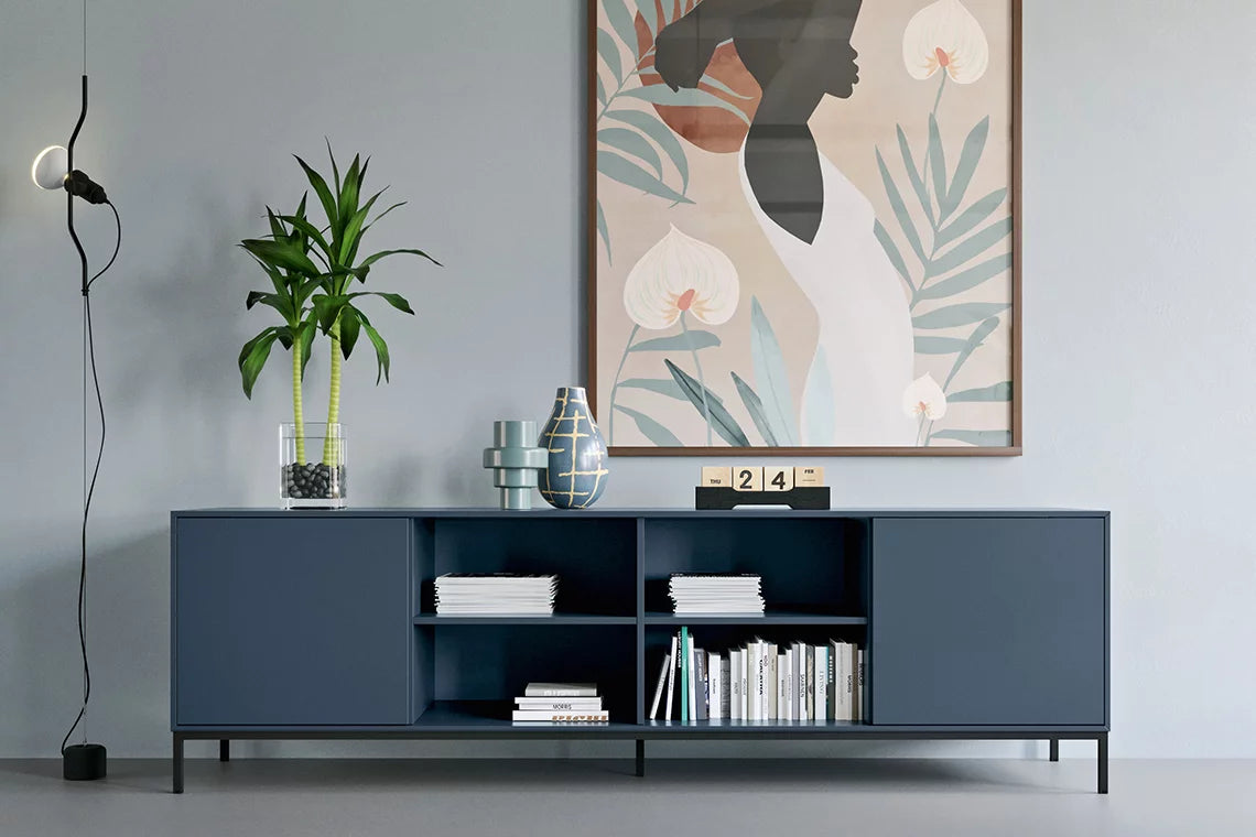 Un salon moderne avec le Buffet Quadra d'Attitudes Bureaux en bleu, des vases décoratifs, des livres, une plante en pot, une lampe murale minimale et une grande œuvre d'art abstraite encadrée représentant une femme avec des feuilles.