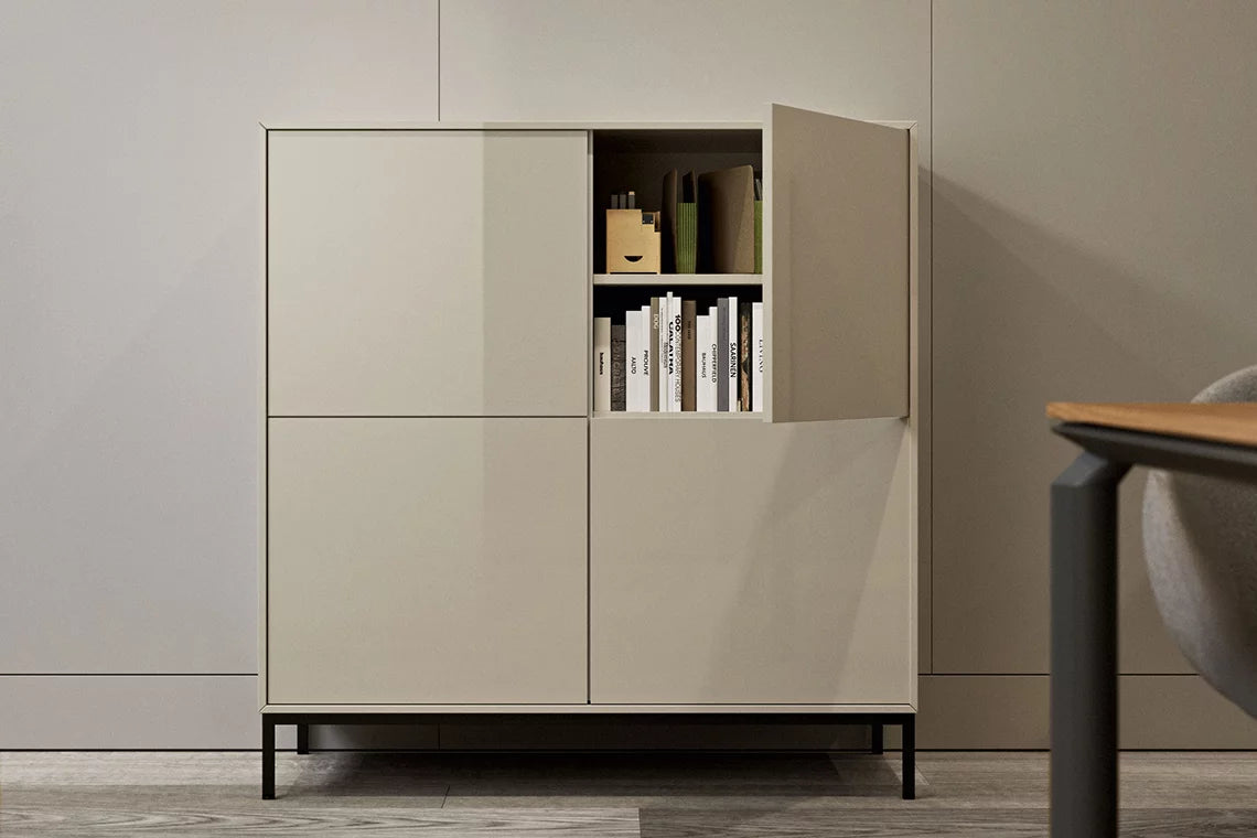 Le Buffet Quadra d'Attitudes Bureaux est composé de quatre compartiments fermés et d'une porte ouverte permettant d'exposer des livres et des petits objets organisés. Il est posé sur des pieds noirs dans une pièce minimaliste aux murs et au sol clairs.