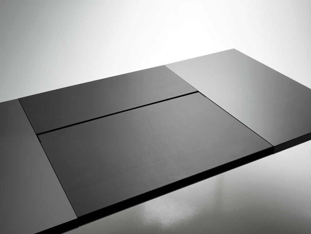 La table Attitudes Bureaux Neta Executive est une table rectangulaire moderne à rallonge, de couleur noire, aux lignes épurées et à la surface lisse, parfaite pour les espaces de travail contemporains. Elle est présentée partiellement déployée sur un sol blanc réfléchissant.