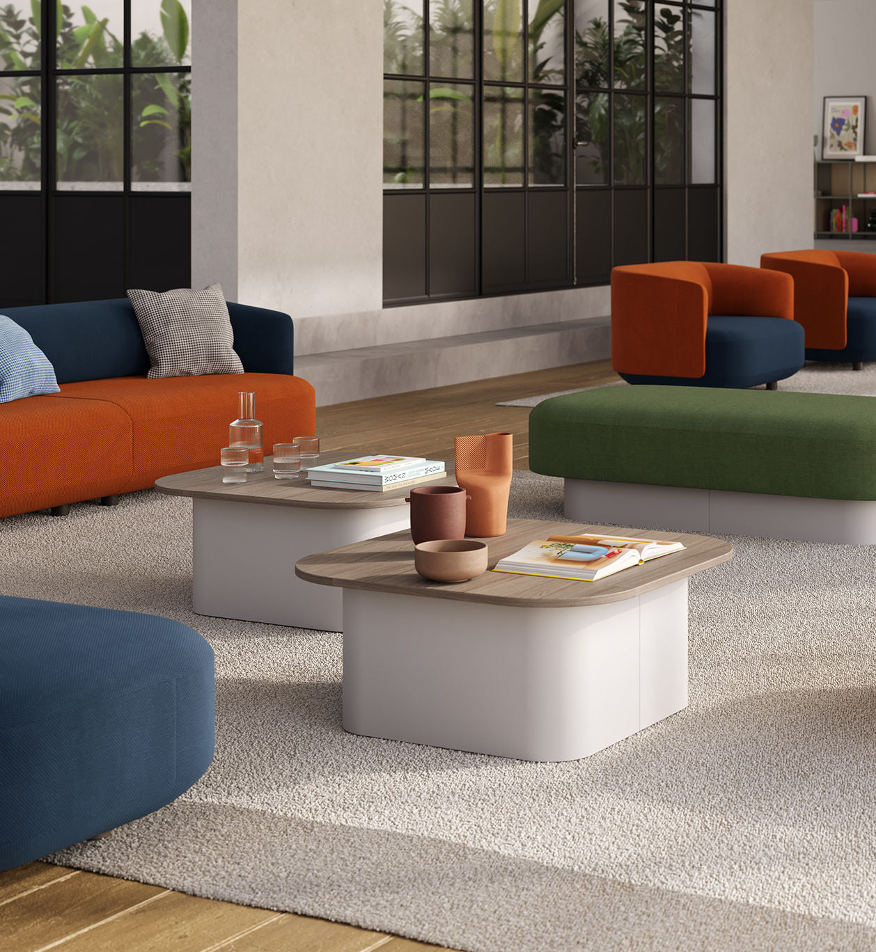 Salon moderne avec canapés rembourrés bleu, orange et vert, Ramos Bassols Tables basses Afina surmontées de vases, de verres et de livres, grandes fenêtres, murs neutres, tapis pelucheux et clair, et verdure luxuriante à l'extérieur.