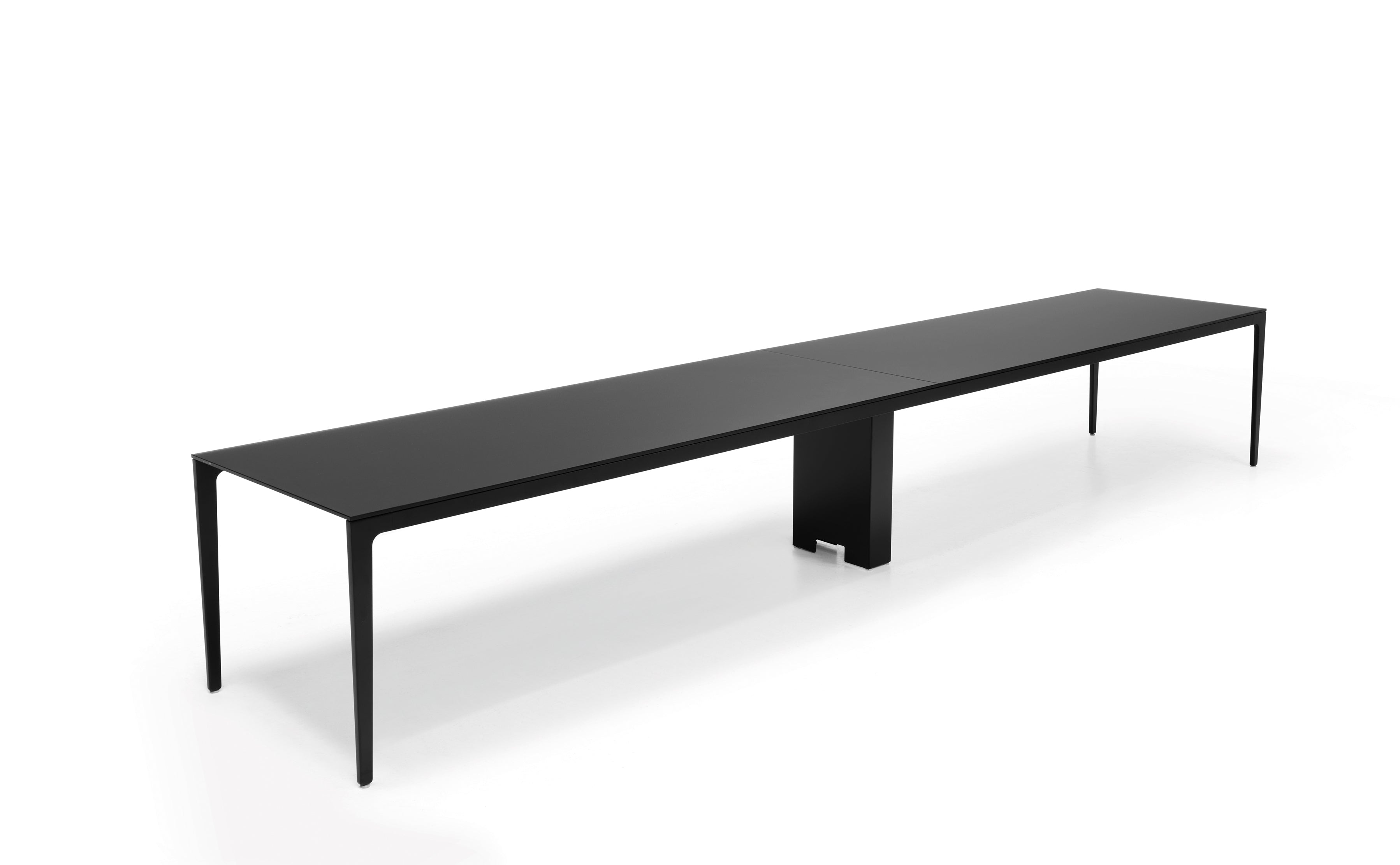 La table de réunion modulables Alplus de Marco Zito est une table rectangulaire noire, moderne et élégante, dotée de pieds élancés et d'un support central, qui met en valeur son système modulaire sur un fond blanc uni.