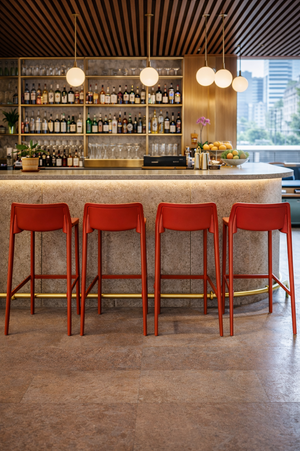 Un bar moderne présente quatre Tabourets ATTIC by Attitudes Bureaux rouges alignés sur un comptoir incurvé, avec des étagères de boissons et de verres derrière, et des lampes suspendues rondes accrochées au plafond.