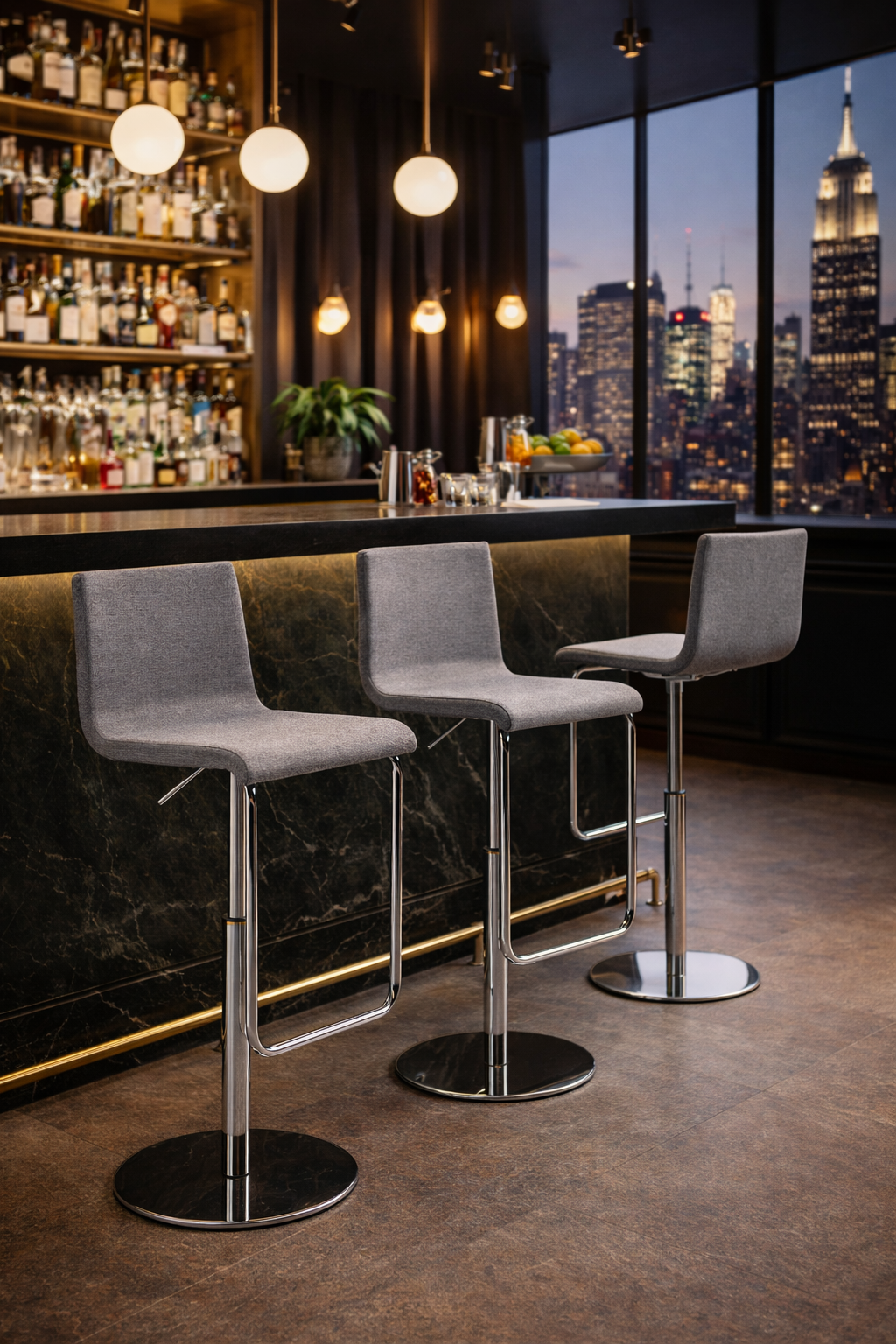 Trois tabourets Tabouret PRINCE d'Attitudes Bureaux, dotés d'une assise grise moderne et d'une base en métal, sont placés devant un bar en marbre noir aux lignes épurées, avec des étagères de bouteilles et de verres. De grandes fenêtres permettent d'admirer la ligne d'horizon de la ville à la tombée de la nuit.