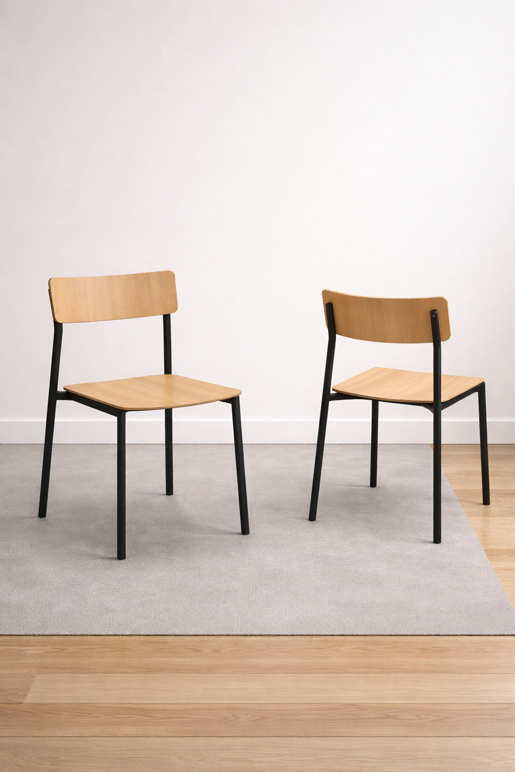 Deux chaises empilables Bois Cult d'Attitudes Bureaux en chêne courbé, pieds en métal noir, sont placées sur un tapis gris clair sur parquet devant un mur blanc-idéales pour un usage professionnel ou domestique.