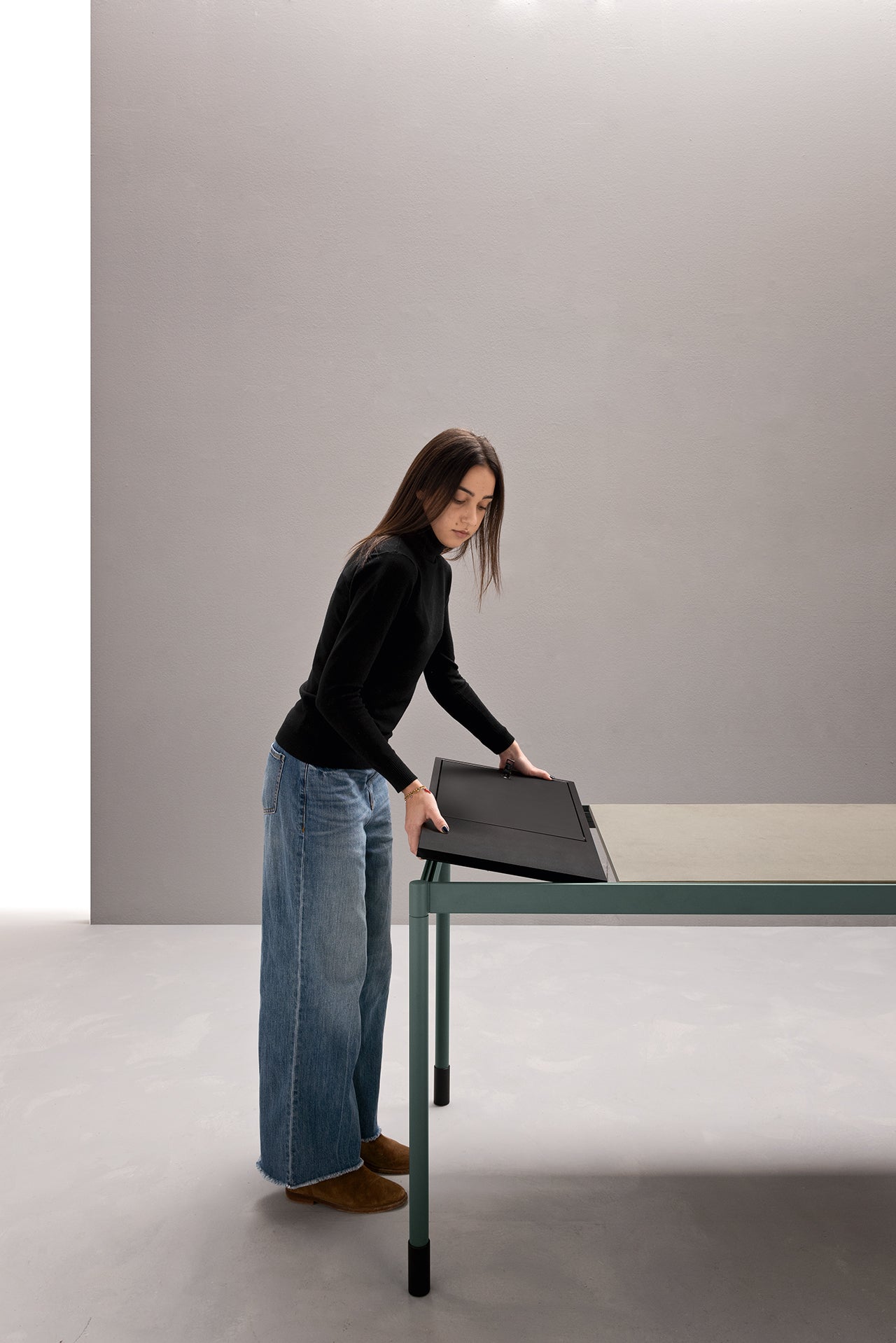 Une femme en col roulé noir et jean large range un dossier noir sur Fluido, mobilier modulaire transformable d'Attitudes Bureaux - un choix parfait pour tout espace minimal grâce à son design reconfigurable.