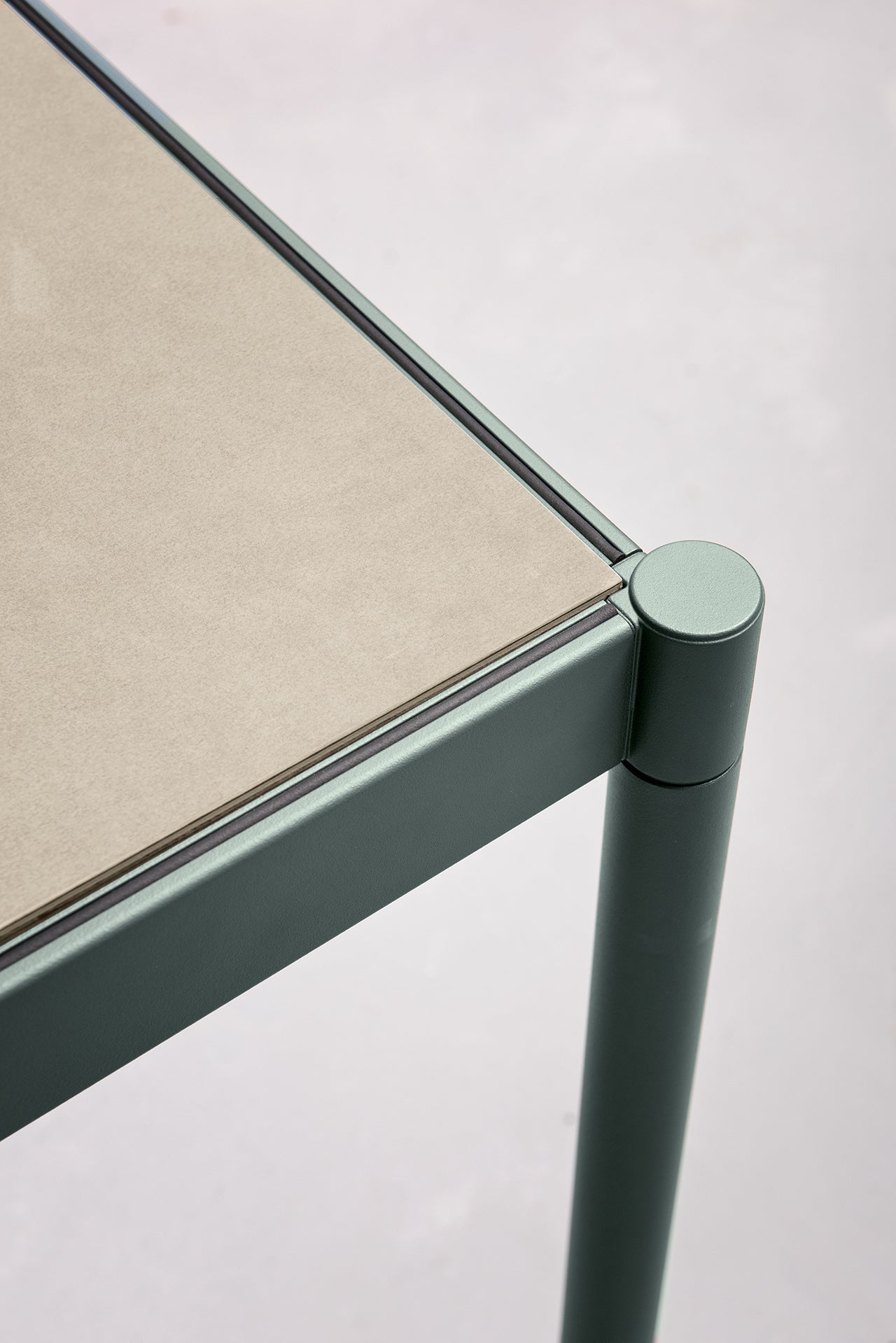 Gros plan sur Fluido, mobilier modulaire transformable d'Attitudes Bureaux : une table moderne avec un plateau beige clair mat et une structure en métal vert aux bords arrondis et aux pieds cylindriques, sur un fond neutre et doux.