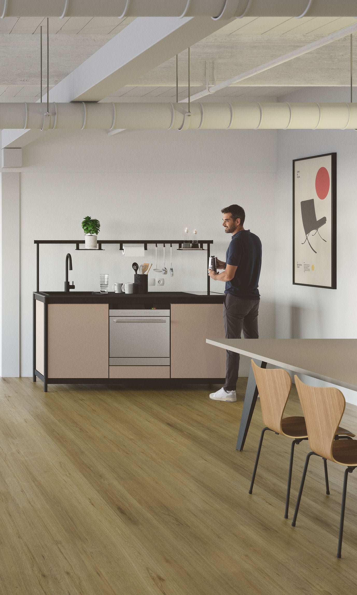 Un homme se sert une boisson dans la kitchenette Fluido® d'Attitudes Bureaux, avec des meubles clairs, des œuvres d'art murales, des sols en bois, des chaises modernes au premier plan et une plante en pot pour une touche minimaliste.