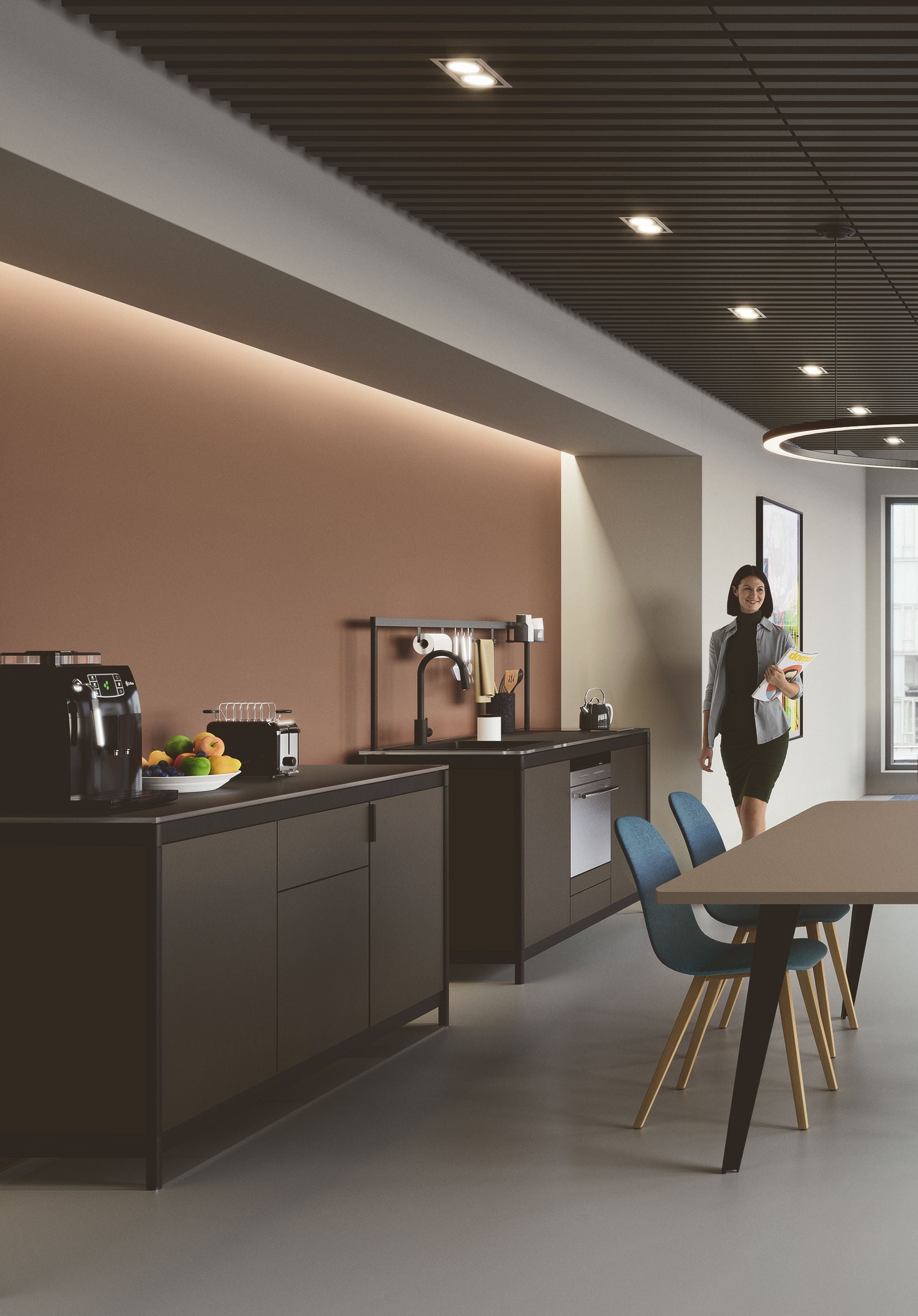 Une kitchenette moderne Fluido® d'Attitudes Bureaux avec des armoires brunes et noires, des appareils encastrés, une machine à café et des fruits sur le comptoir. Une femme d'affaires marche près d'une table à manger avec des chaises bleues, idéale pour un espace de pause au bureau.