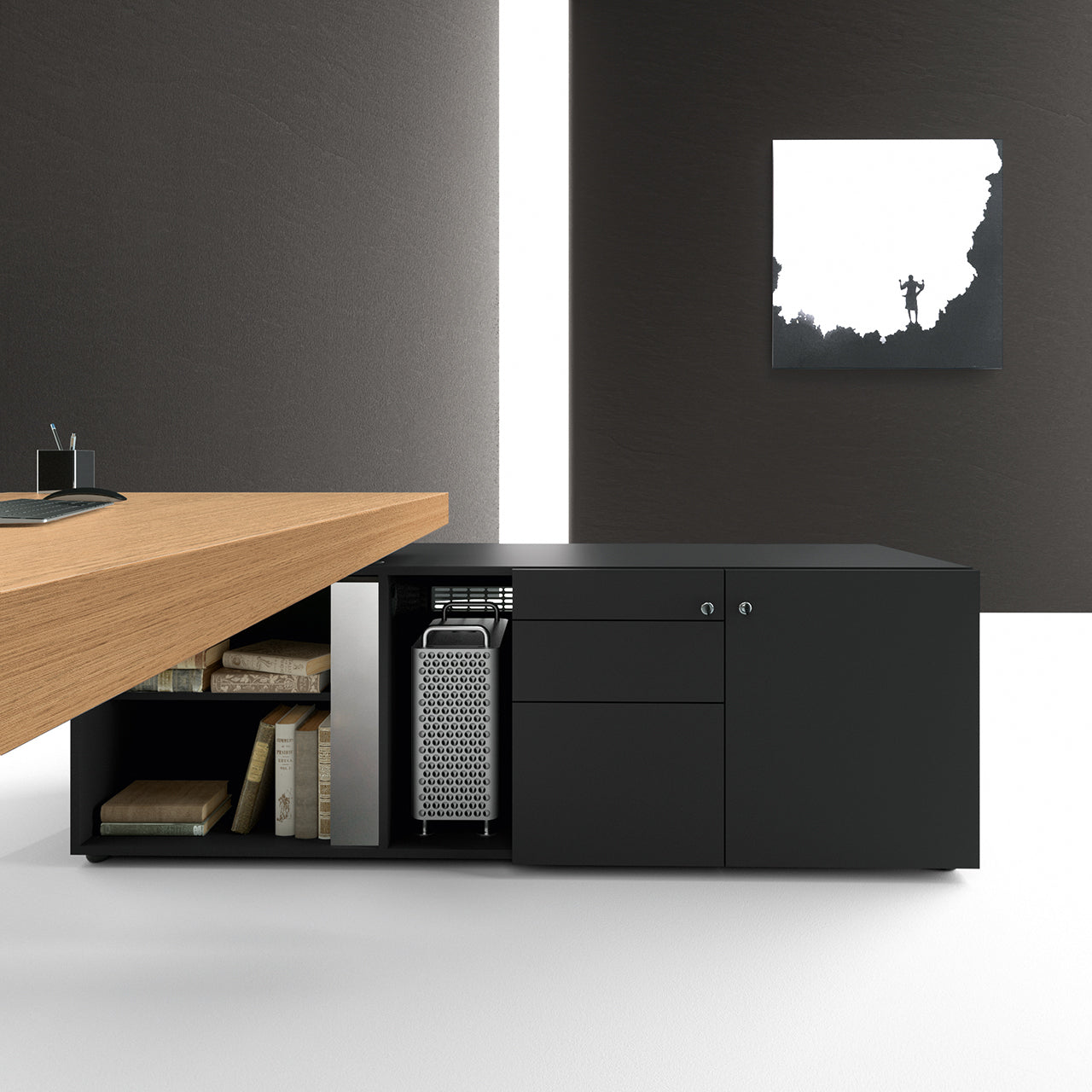 Dans un bureau moderne, le bureau en bois Kyo et le meuble d'appoint noir d'Attitudes Bureaux contiennent des livres. Le décor minimaliste comprend des murs sombres, un mur blanc avec de l'art abstrait, et met en valeur des bureaux directionnels et des matériaux haut de gamme.