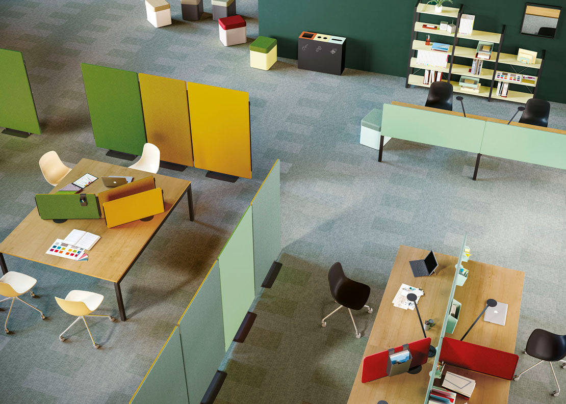 Bureau ouvert moderne avec bureaux en bois clair, Cloisons et écrans acoustiques MADISON d'Attitudes Bureaux comme pare-vue colorés, chaises de bureau, livres et ordinateurs portables. Des cubes de rangement et des étagères s'alignent sur les murs verts pour créer un espace de travail lumineux et organisé.