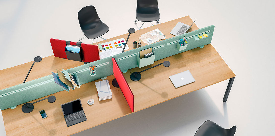Un espace de travail moderne avec deux bureaux en bois reliés par une cloison verte et des cloisons et écrans acoustiques rouges MADISON par Attitudes Bureaux, avec des ordinateurs portables, des cahiers, des fournitures de bureau et des chaises noires pour des espaces de travail modulables et flexibles.