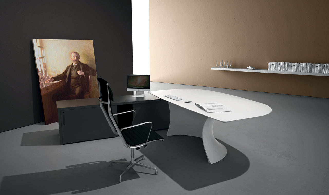 Un bureau moderne et minimaliste présente le bureau blanc incurvé Ola d'Attitudes Bureaux, une chaise noire et argentée, un ordinateur et des livres. Un grand portrait est adossé au mur sombre ; une étagère flottante avec des lunettes et des livres met en valeur le mur beige.