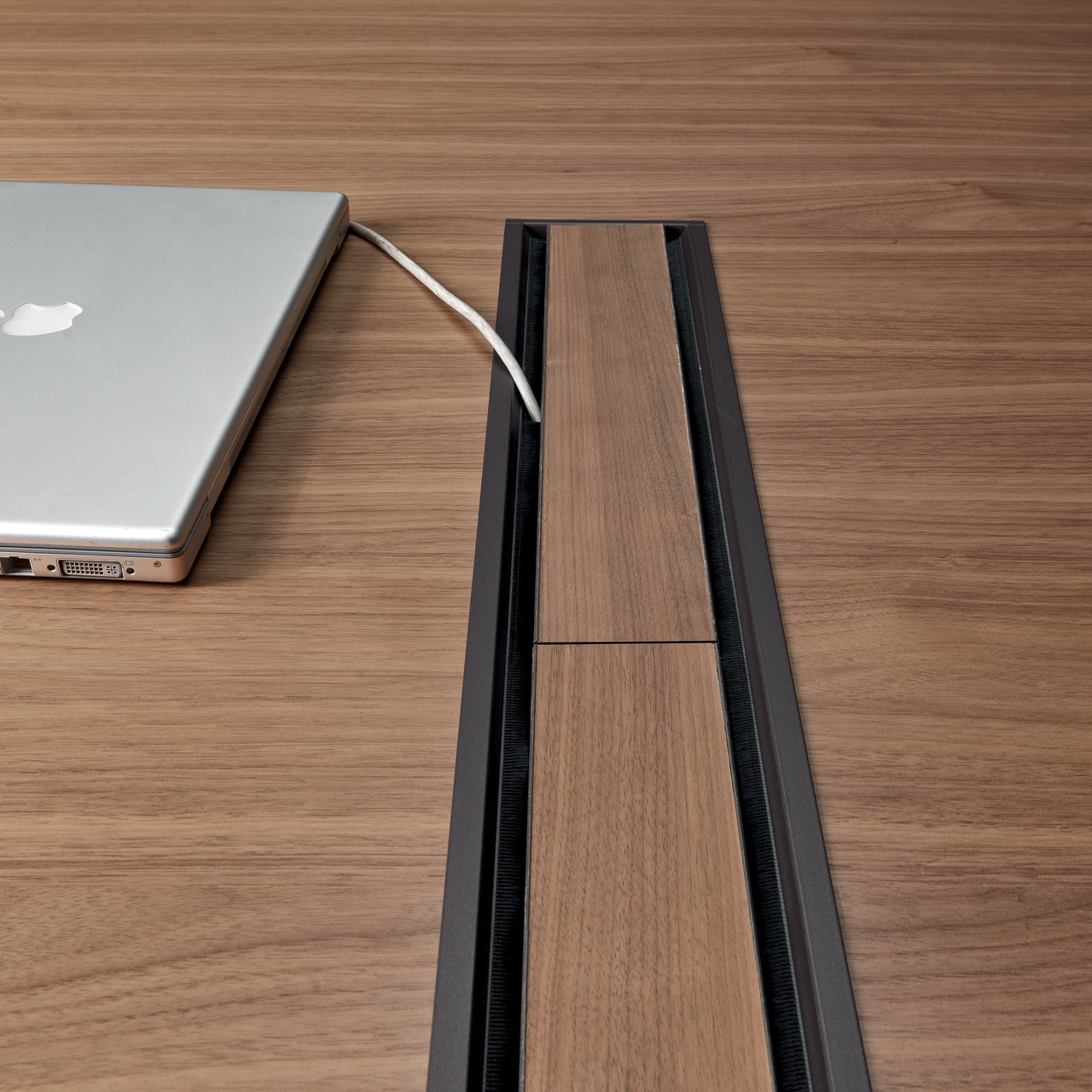 Un ordinateur portable argenté Attitudes Bureaux Ola avec un câble blanc repose sur une table sculpturale en bois avec un système de gestion des câbles intégré et un couvercle en bois assorti.