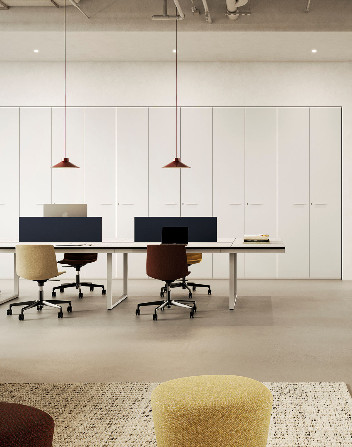 Un espace de bureau moderne présente Attitudes Bureaux Armoires de bureau Passepartout, une longue table avec des panneaux de séparation noirs, des chaises à roulettes marron et jaunes, des ordinateurs portables sur des bureaux et deux lampes suspendues rouges au-dessus de la tête.