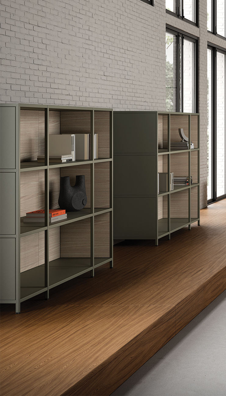 Le bureau Attitudes Bureaux Bibliothèque de bureau modulaire Phylo, agrémenté de décorations et de livres, est adossé à un mur de briques blanches et à de grandes fenêtres. Des étagères et un sol aux tons sourds complètent cet intérieur moderne et design.