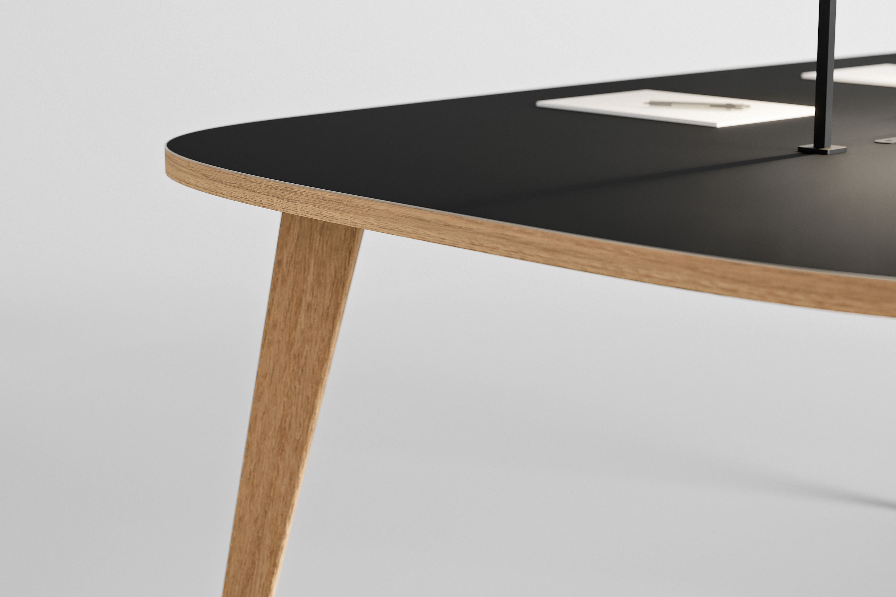 Un gros plan de la table Mobilier de direction Pigreco d'Attitudes Bureaux montre sa surface noire, son bord en bois clair, son pied en bois incliné et ses prises électriques blanches intégrées sur un fond clair et uni.
